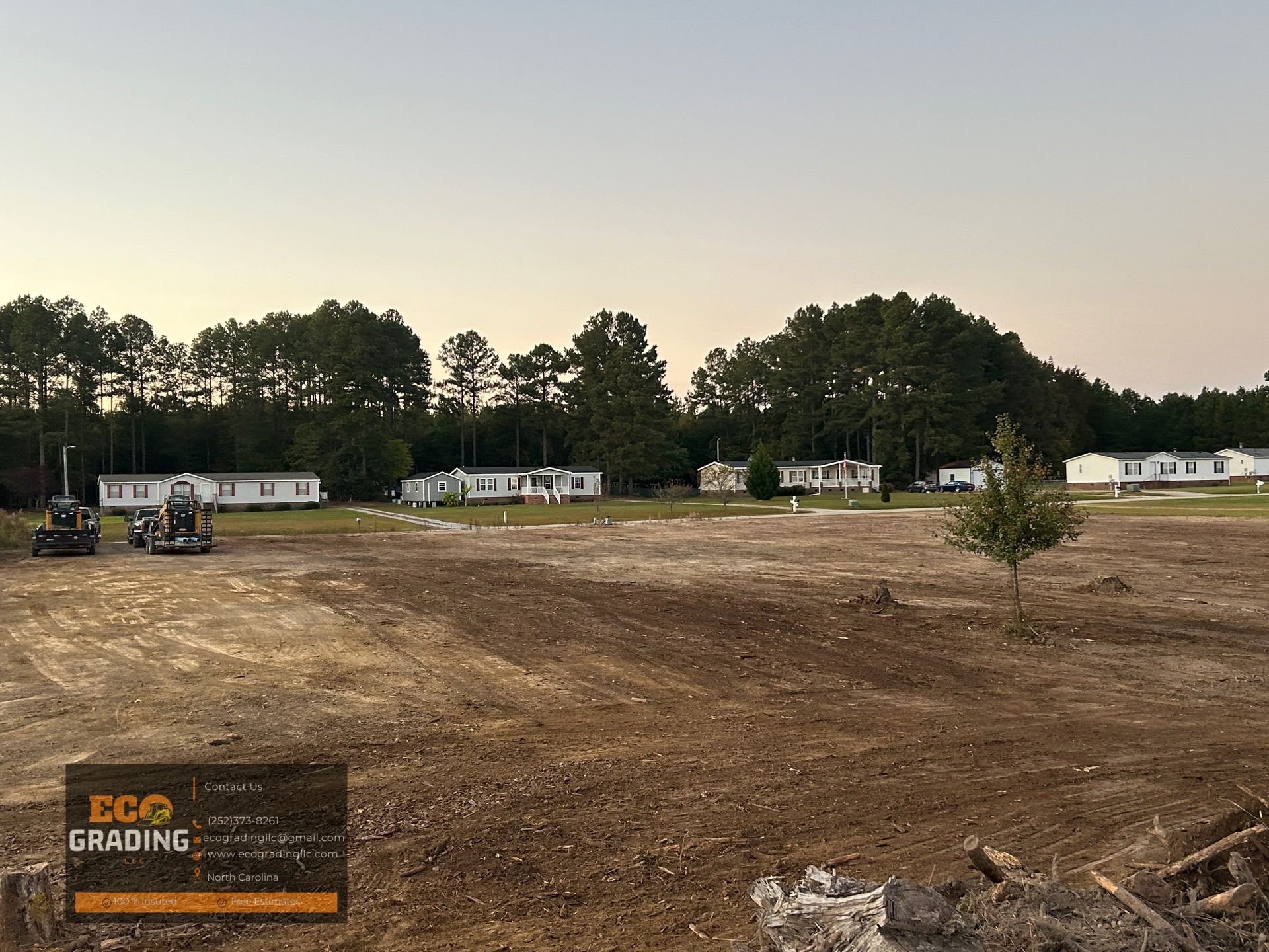 A cleared construction site with mobile homes in the background. Dusk sky.
