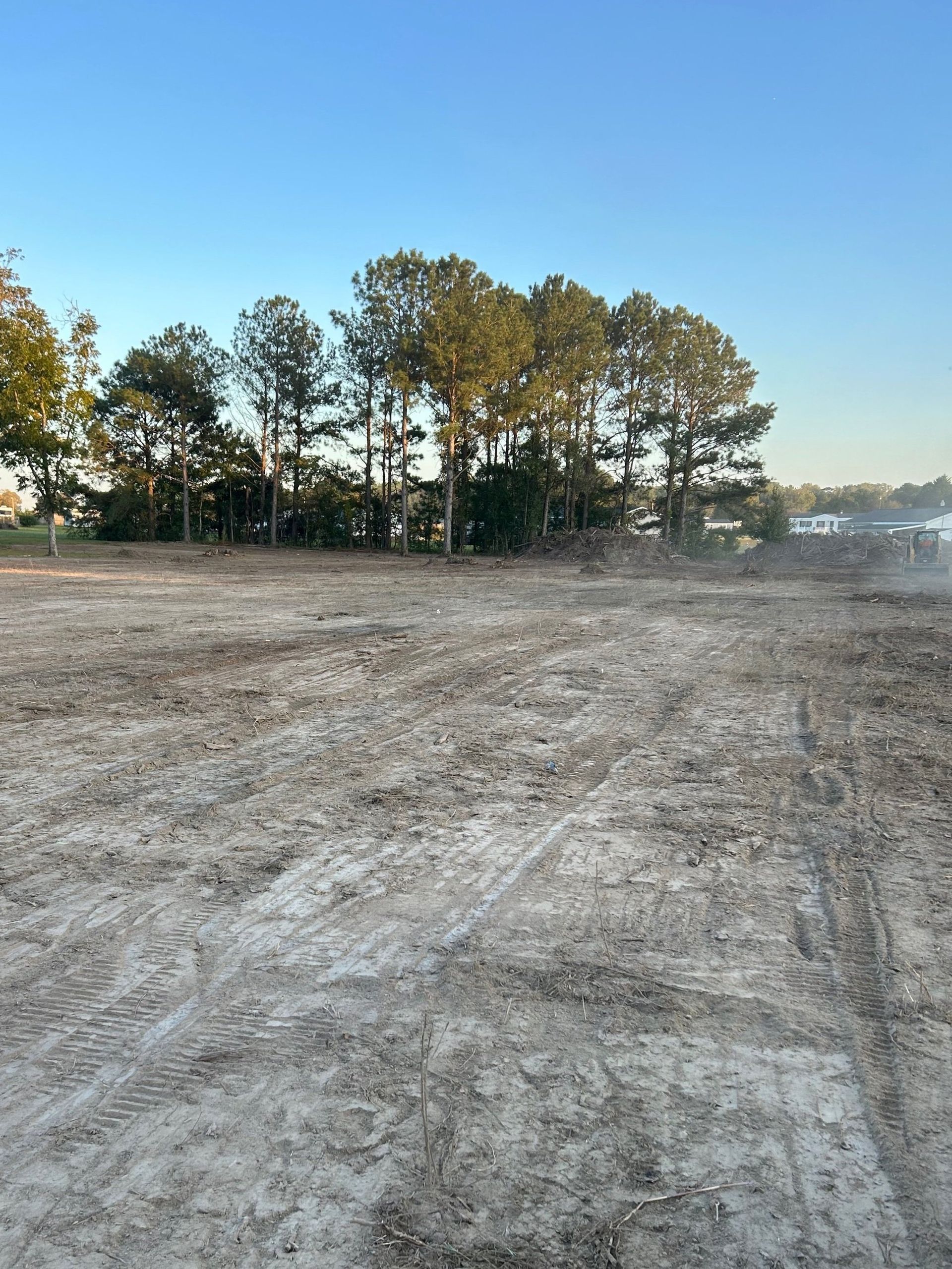 Cleared dirt lot with tire tracks, trees in the background, under a blue sky.