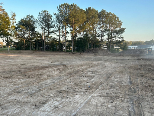 Cleared land with tire tracks, trees in the background, and a building on the right.