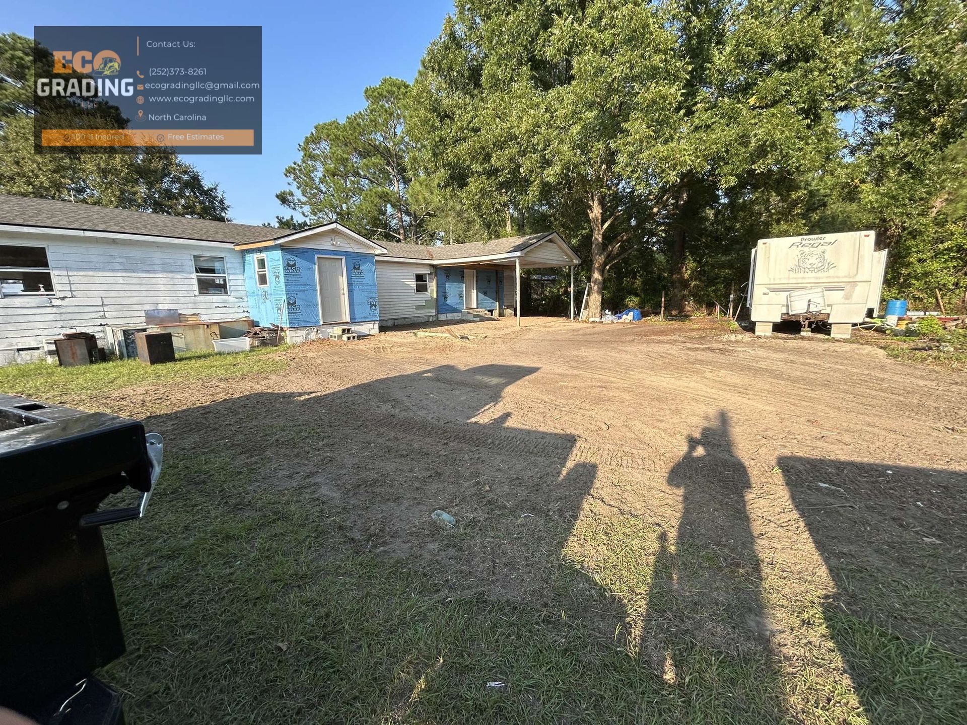 Exterior view of dilapidated buildings and gravel yard with trees in the background.