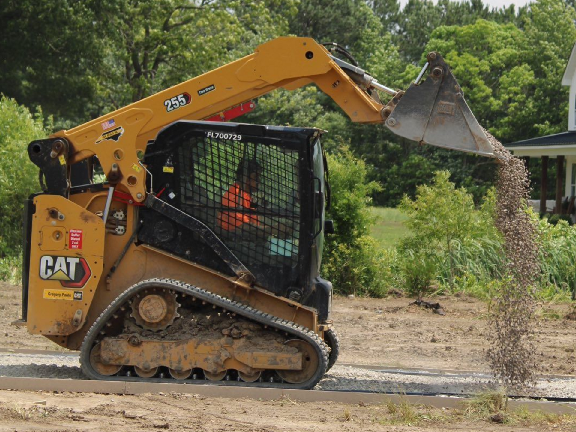 Yellow CAT skid steer dumping gravel on a construction site.