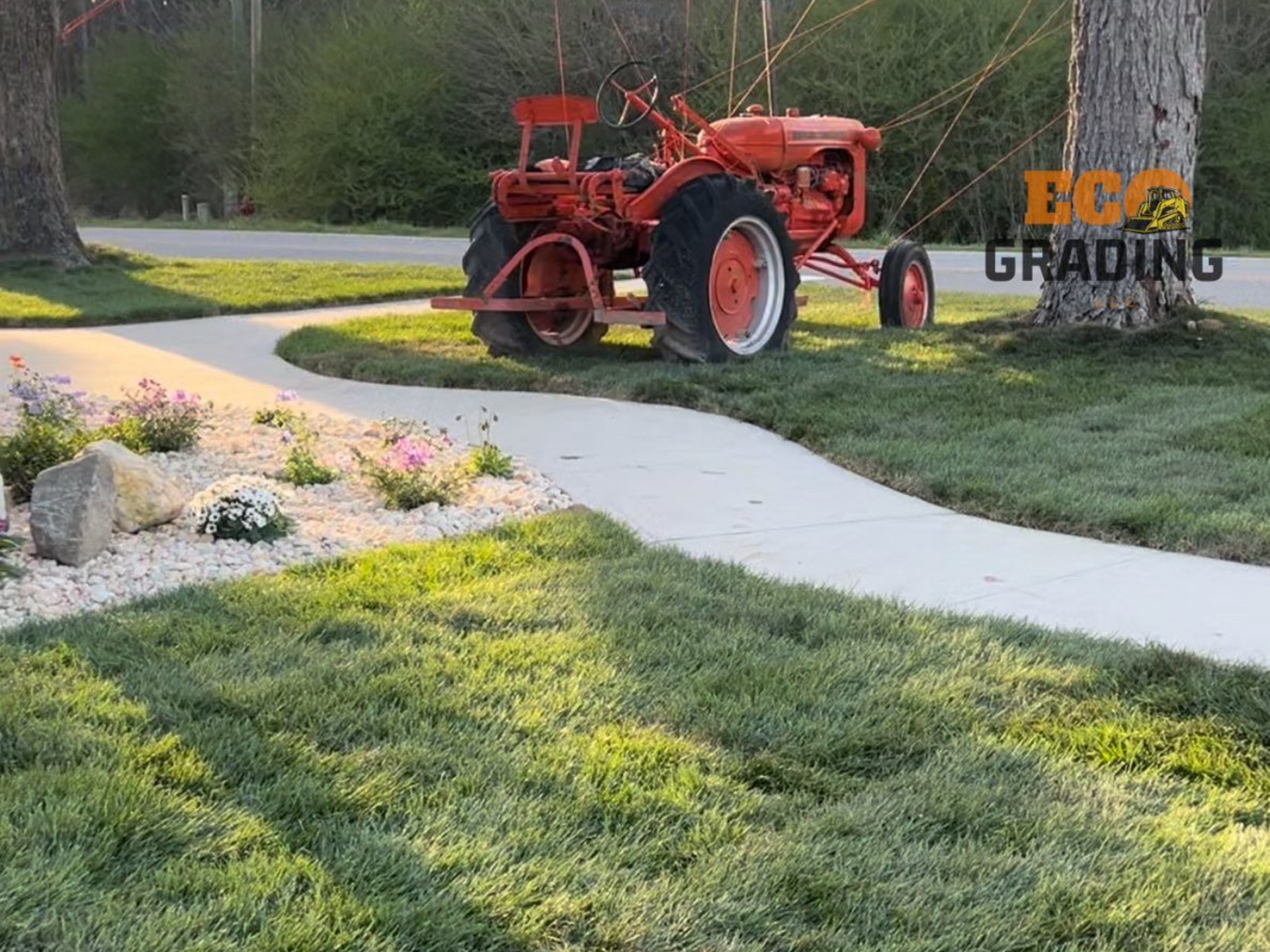 Red tractor parked near a curved sidewalk and tree on a sunny lawn.