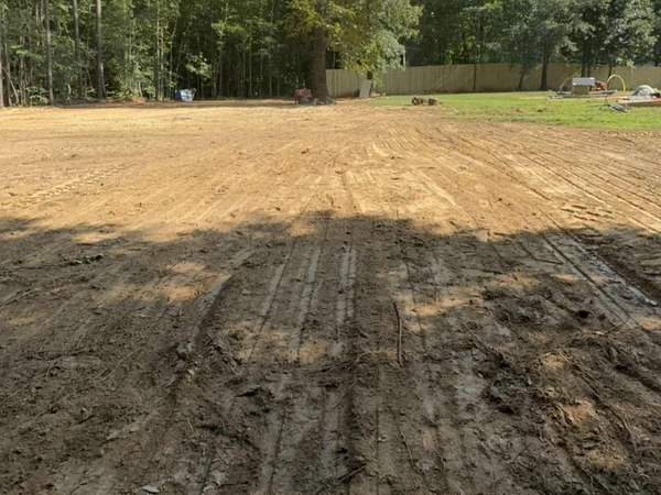 A cleared dirt lot, likely prepared for construction, with tire tracks and trees in the background.