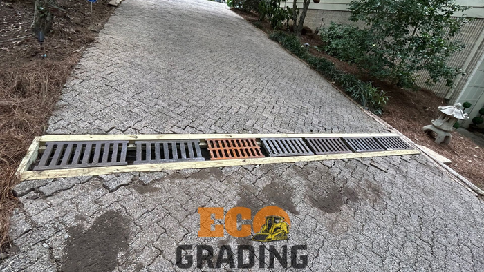 Gravel driveway with a rectangular drainage grate that has a missing section.