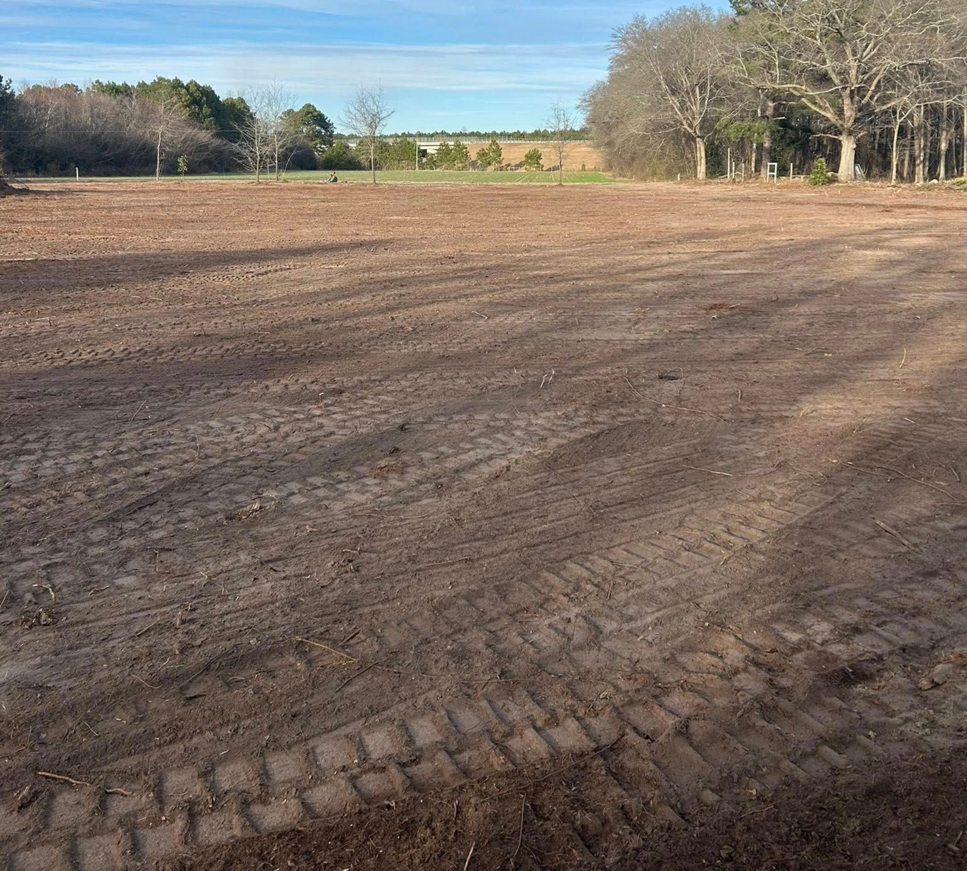 Cleared brown field under a partly cloudy sky, with trees in the background.