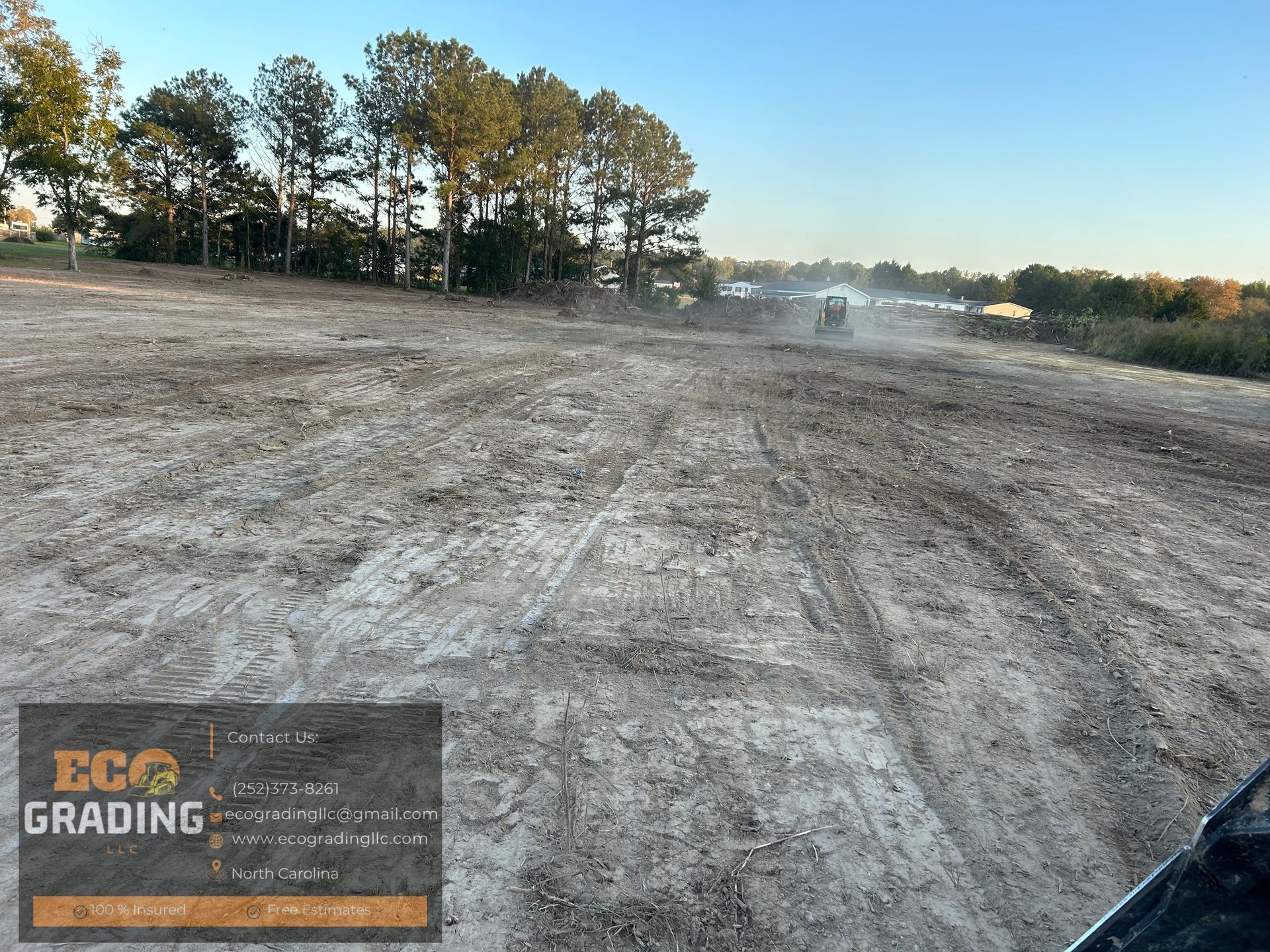 A construction site, dirt and vehicle tracks. Trees in the background. 