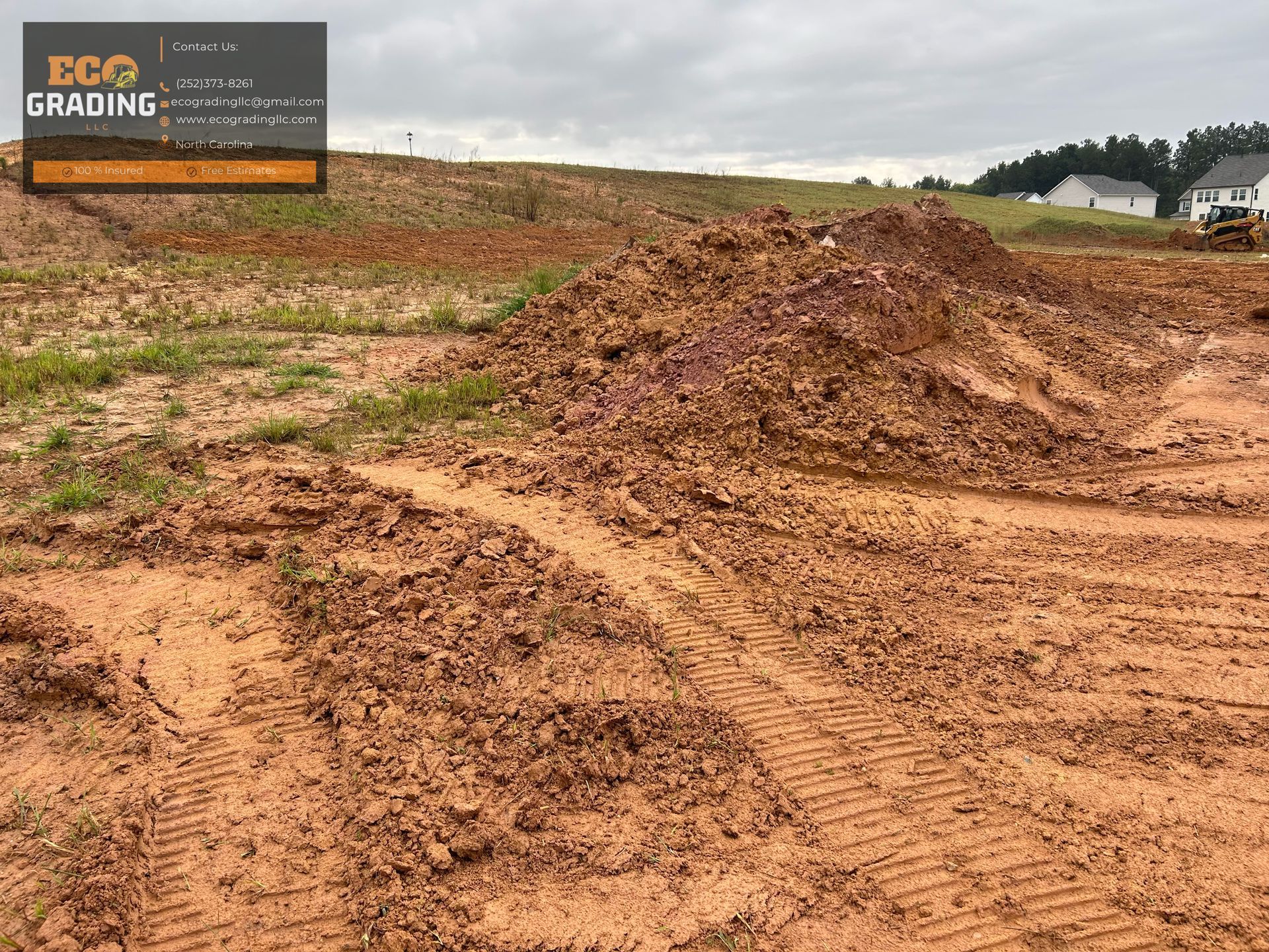 Graded dirt lot with tire tracks. A mound of red clay sits in the center. Gray sky.