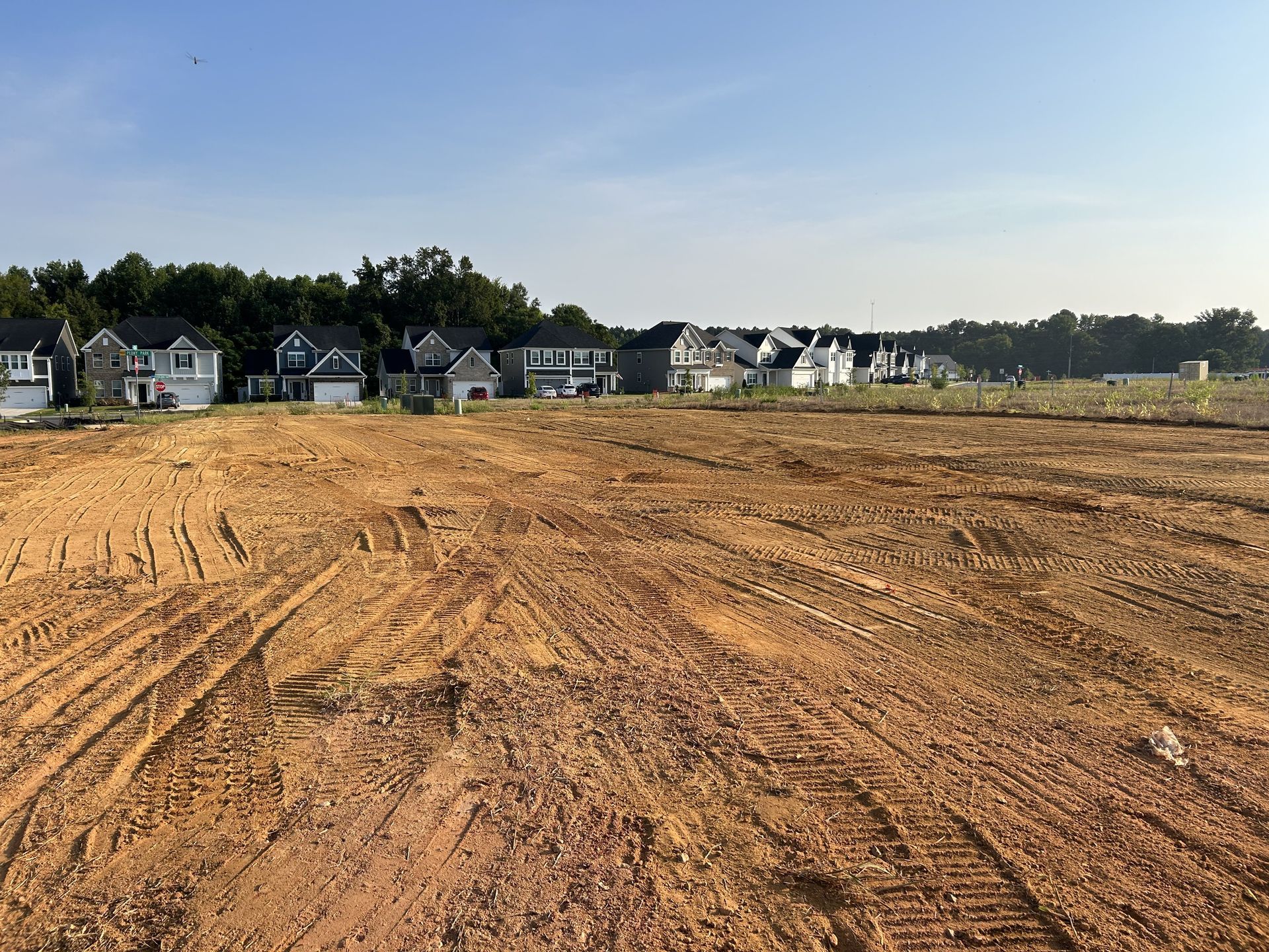 Cleared land with tire tracks, houses in background, blue sky.