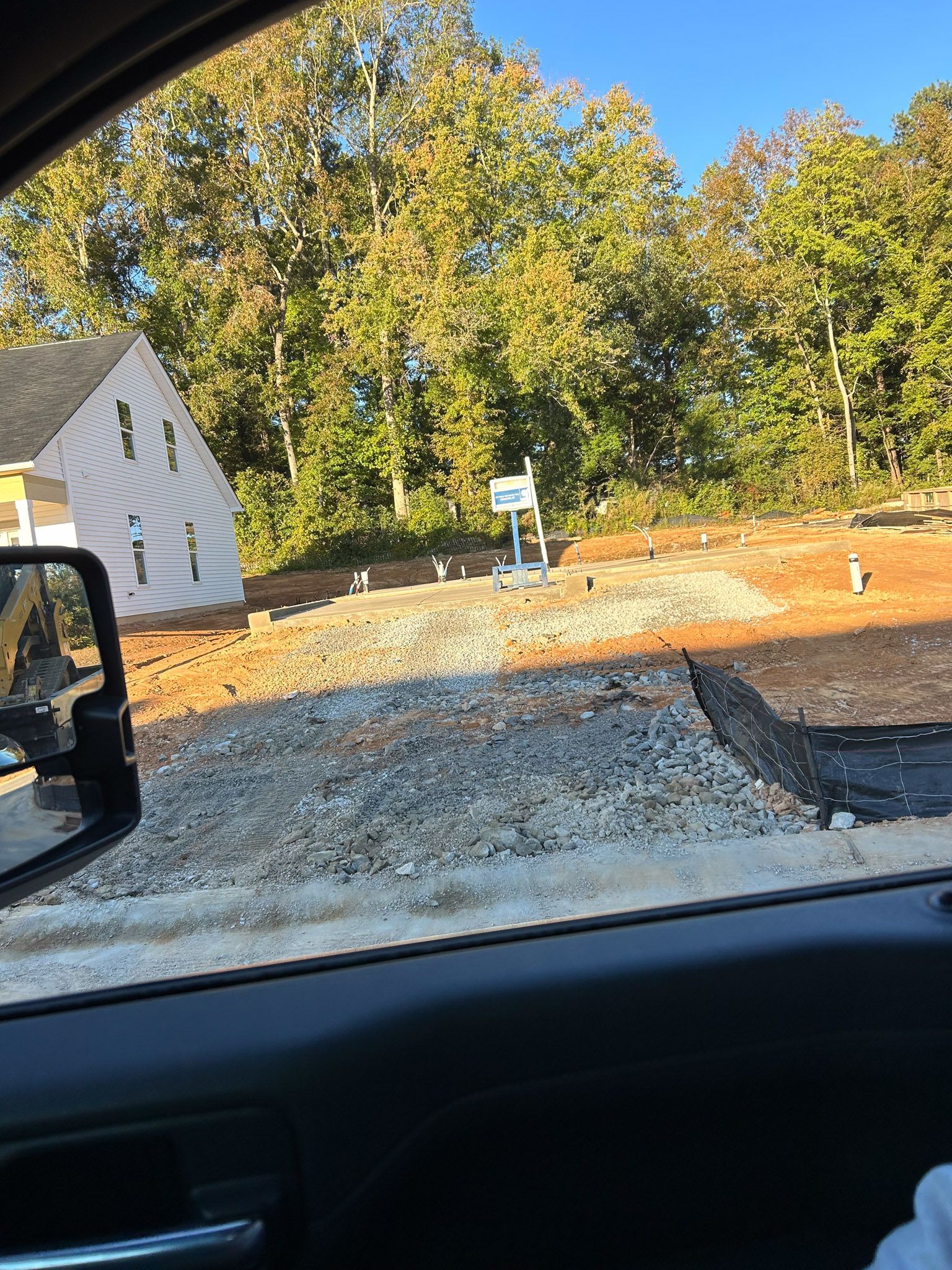 Construction site with new house and gravel driveway. Trees and sky in the background.