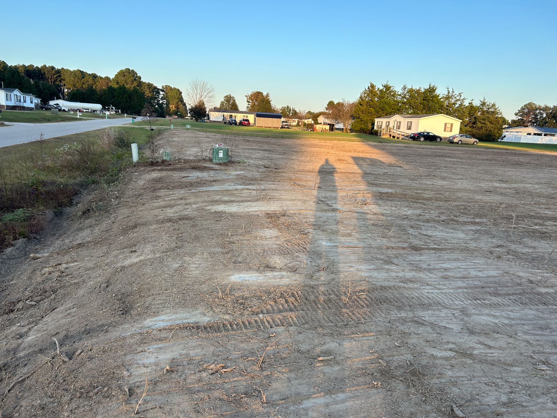 Cleared vacant lot with tire tracks, houses in background under blue sky.