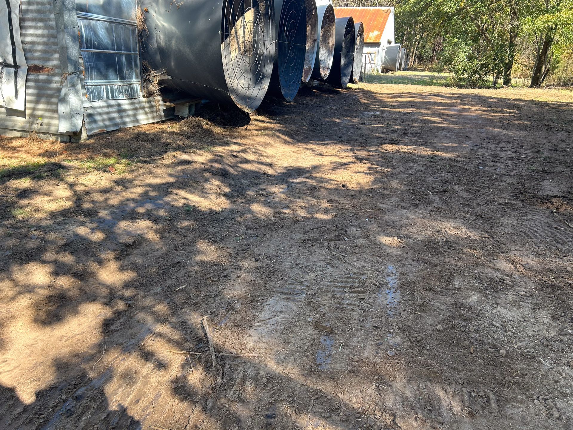 Large metal tanks sit on a dirt lot. Buildings and trees are in the background.