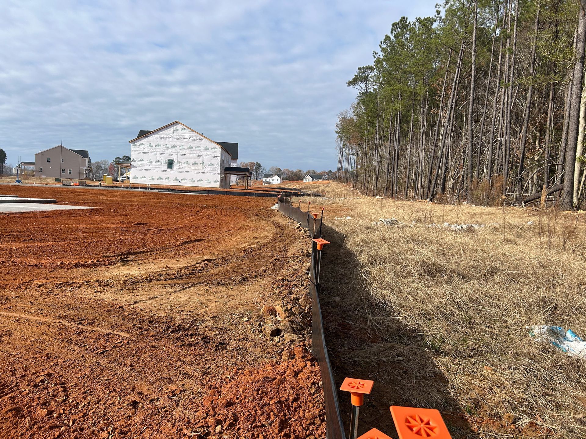 Construction site with red earth, silt fence, and new houses under construction.