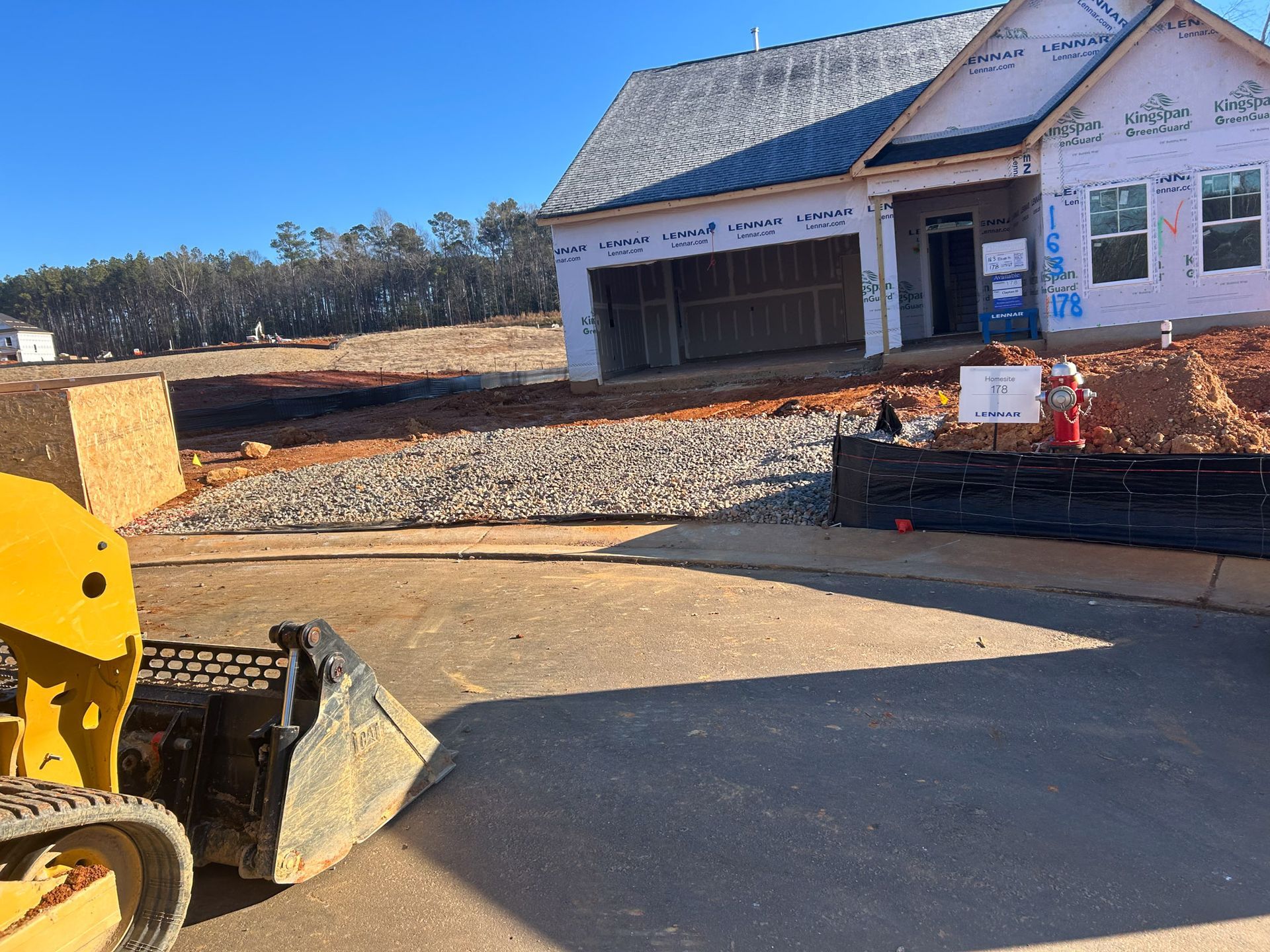 Construction site with a partially built house, gravel, and a yellow loader on a sunny day.