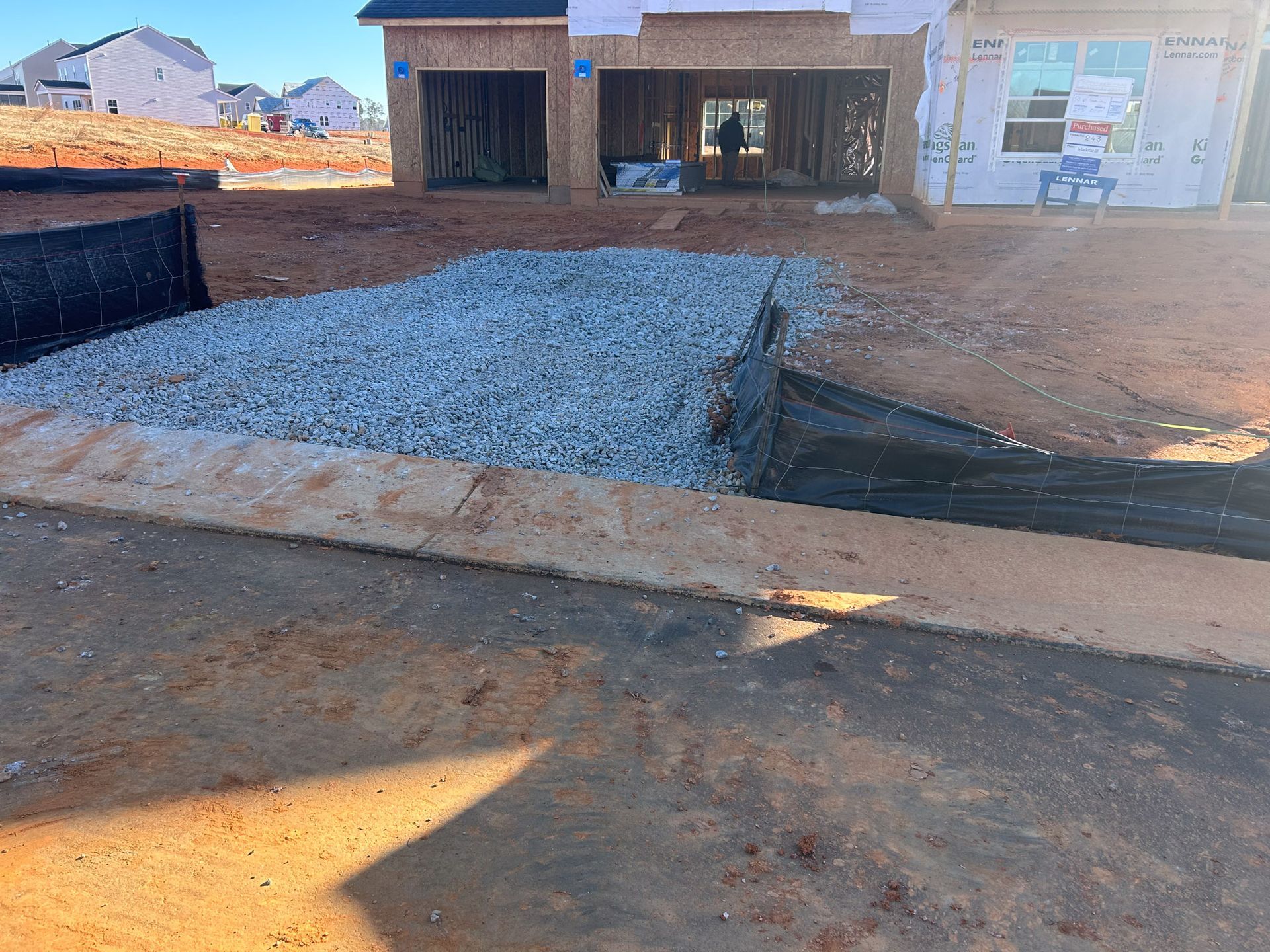 Construction site: gravel driveway, silt fence, partially built house.