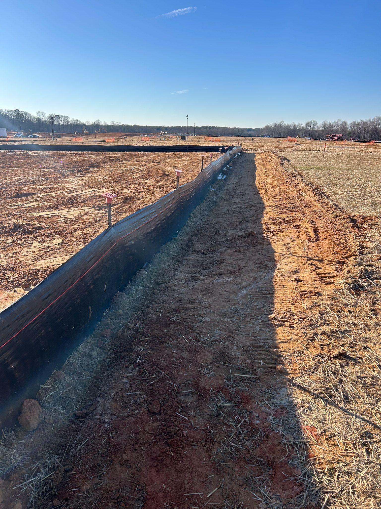 Construction site with black silt fence; brown earth; clear, sunny sky.