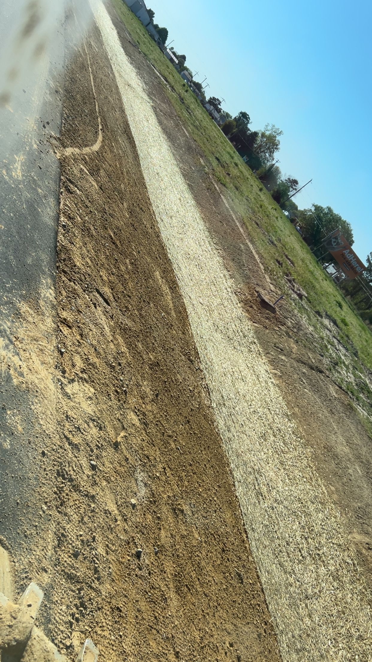 A road with a white stripe down the center and dirt/grass on the sides. Blue sky.