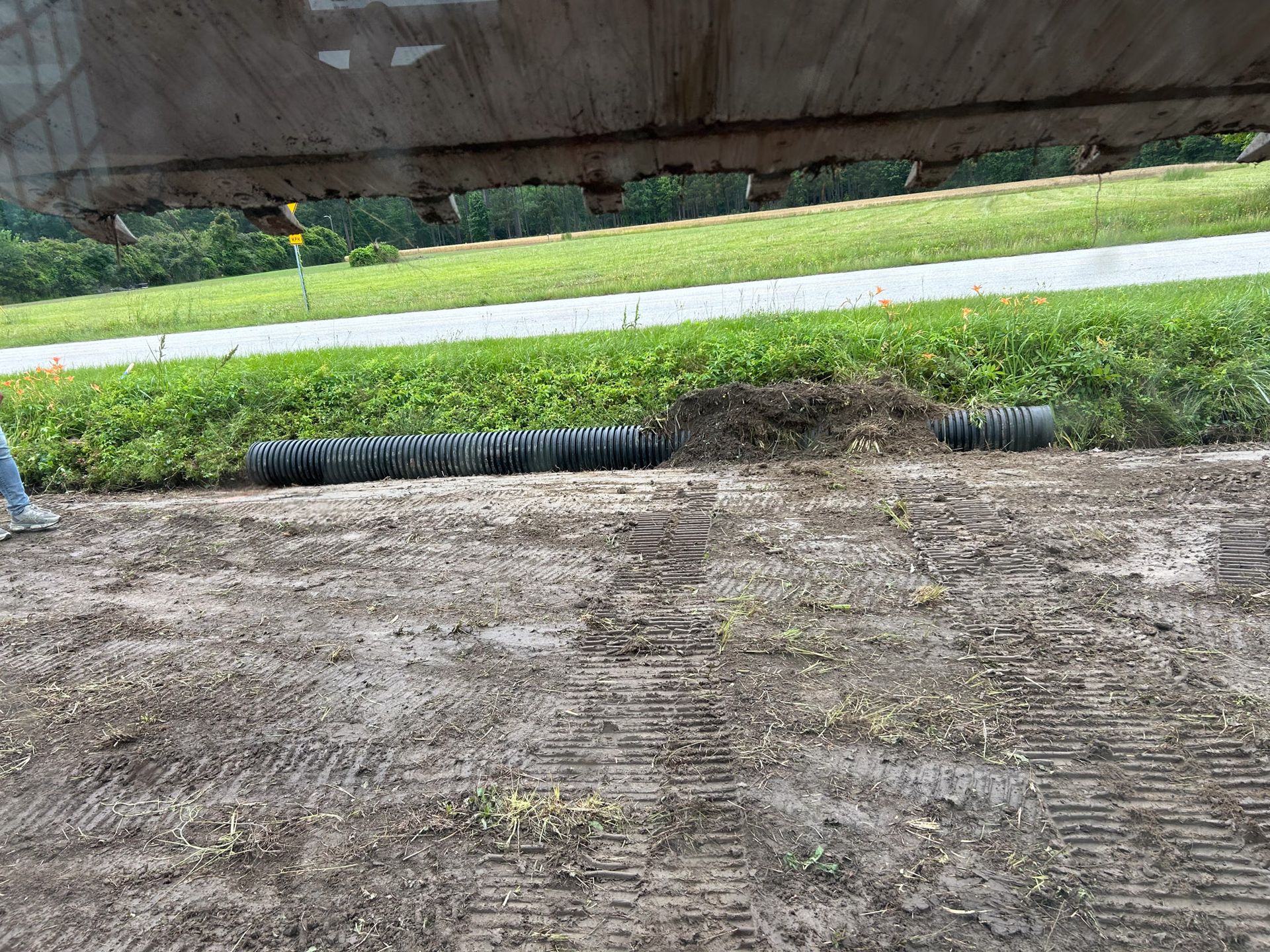 Black corrugated drain pipe runs through grass and dirt near a roadway.