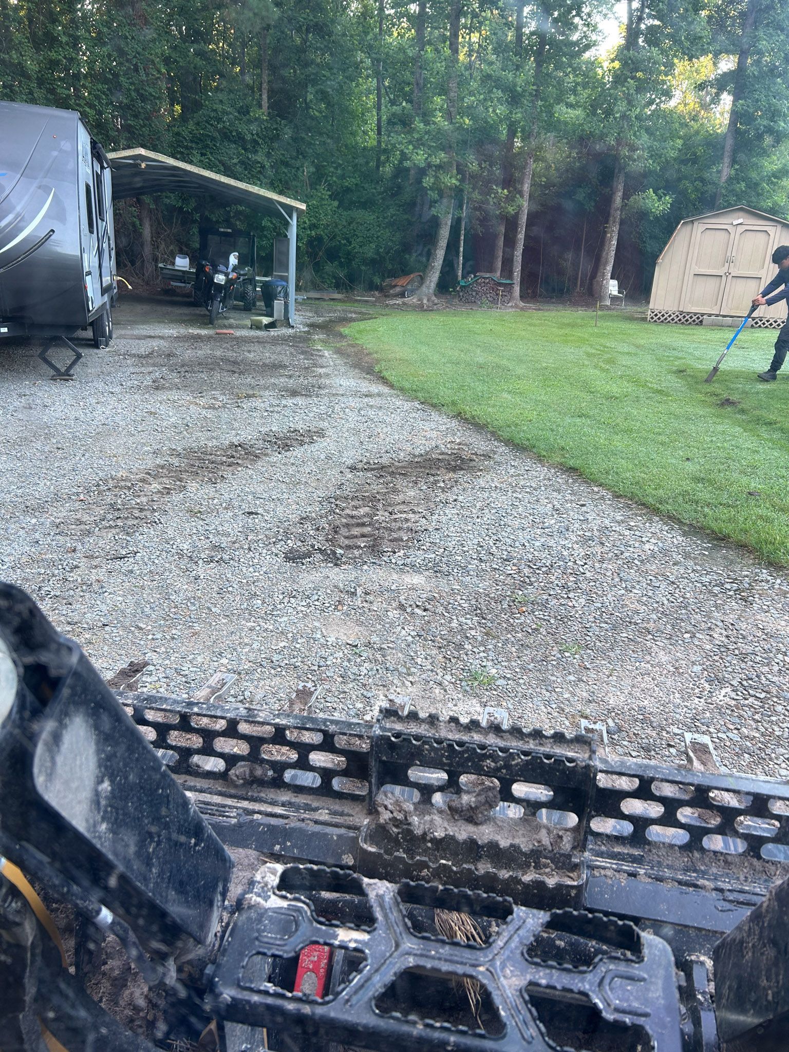 ATV on gravel path, RV, shed, person weeding grass. Green lawn, trees in background.