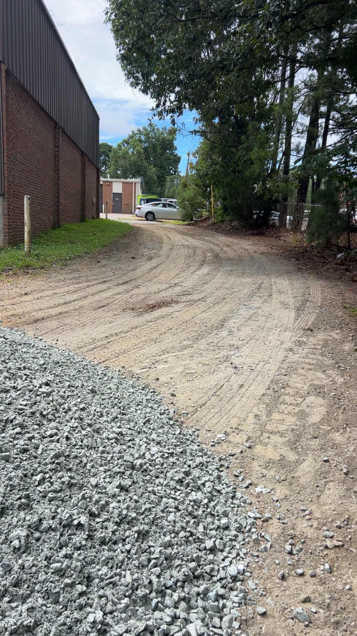Gravel path next to a building, leading toward trees and a vehicle.