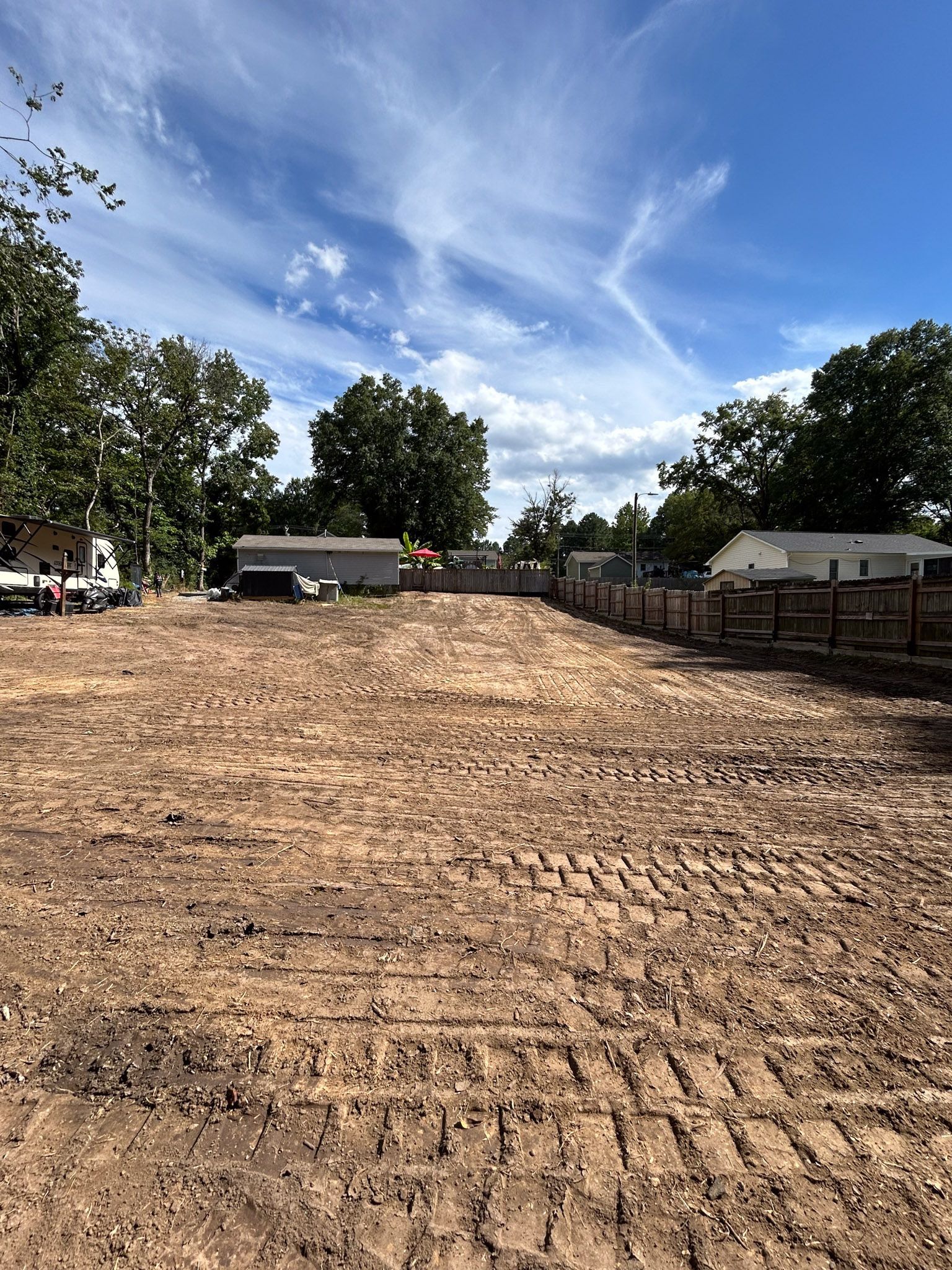 Cleared dirt lot under a blue sky with some clouds; a wooden fence runs along the right side.