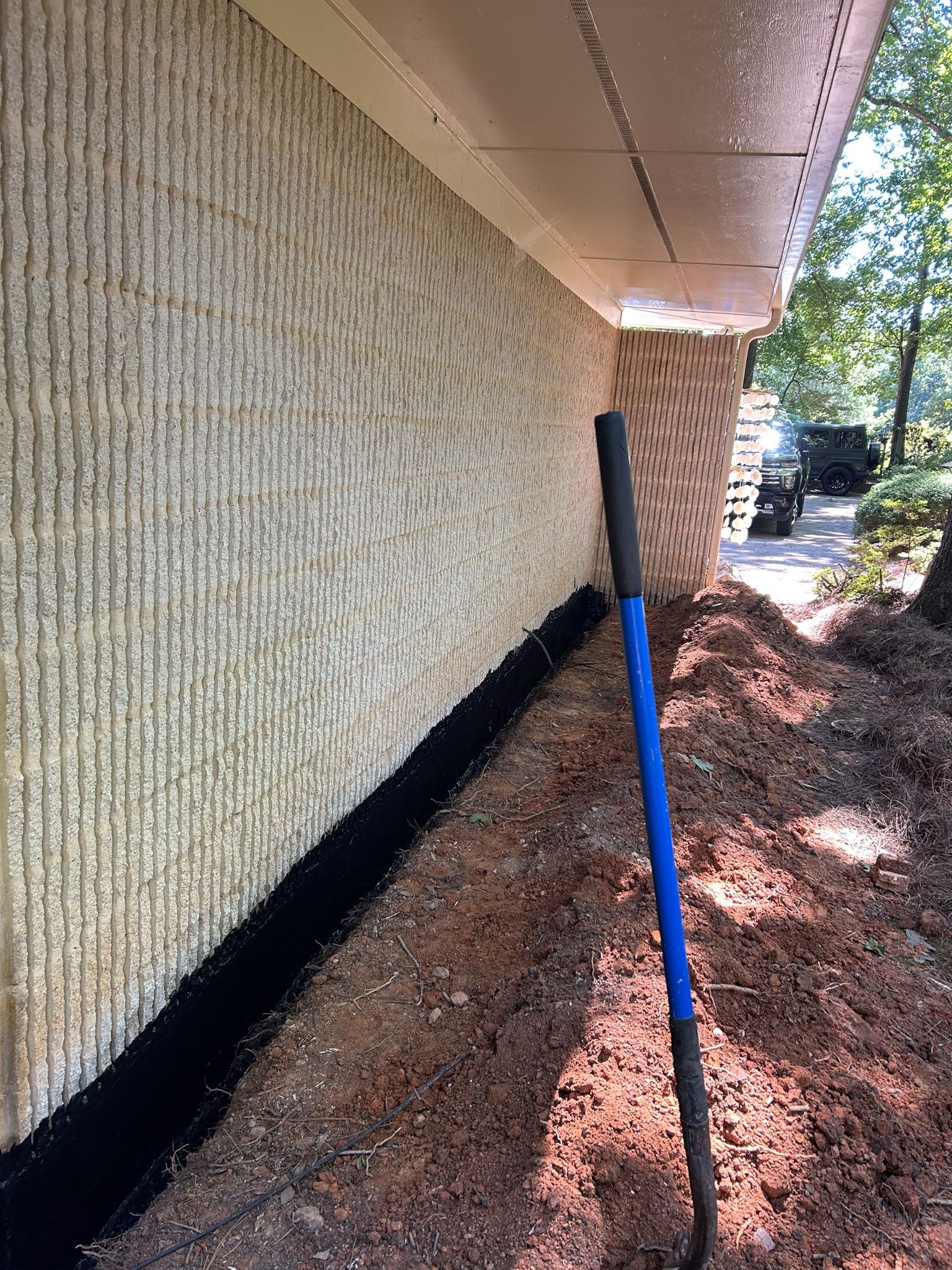 Shovel leaning against a house with textured stucco wall and black lining along the base.