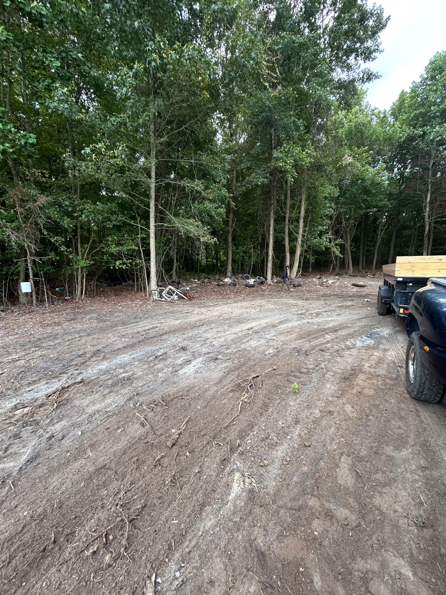 Dirt driveway leading into a tree line. A truck with trailer is parked on the right.