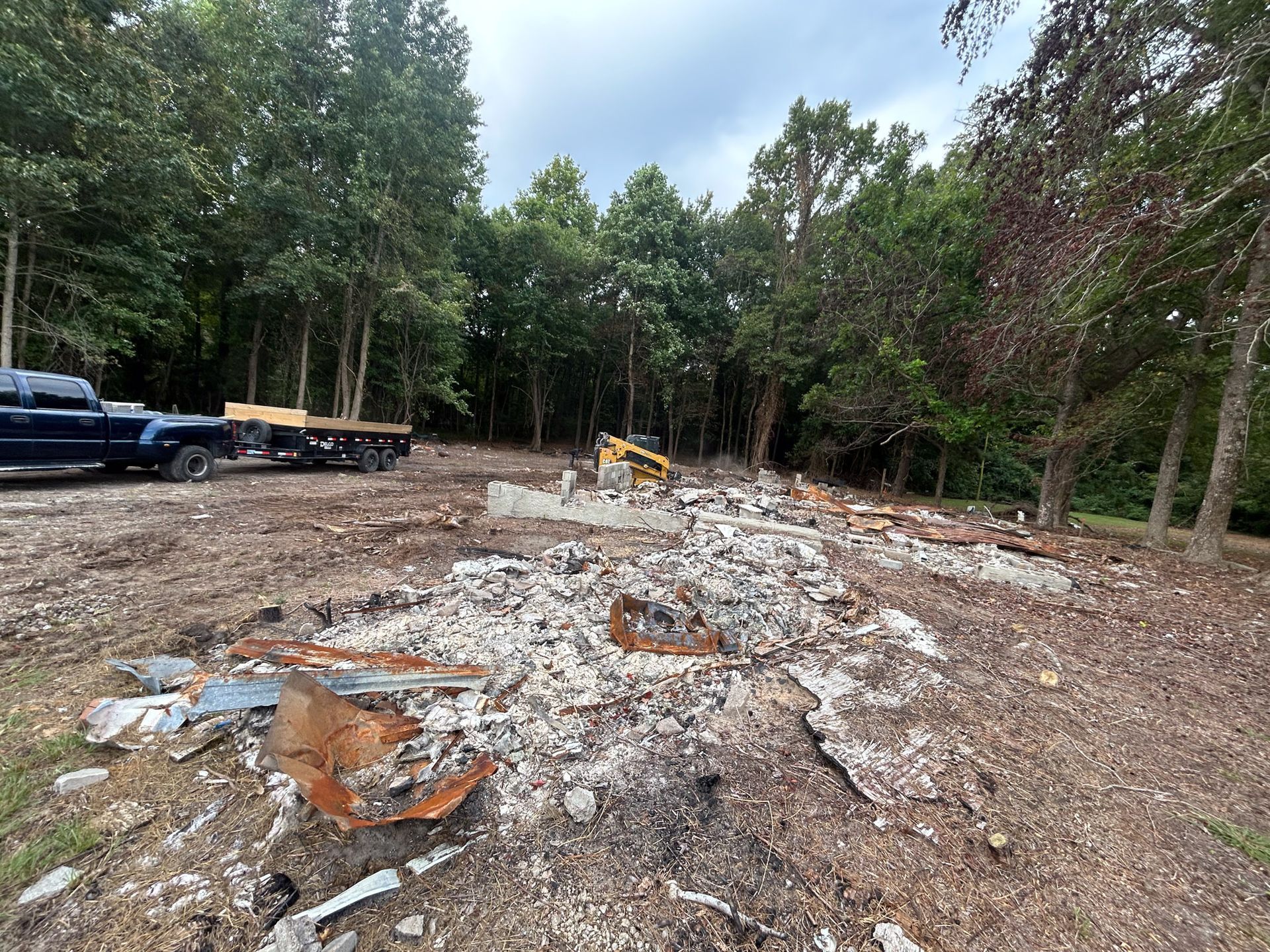 Demolished building site with debris; a truck and trees are visible in the background.
