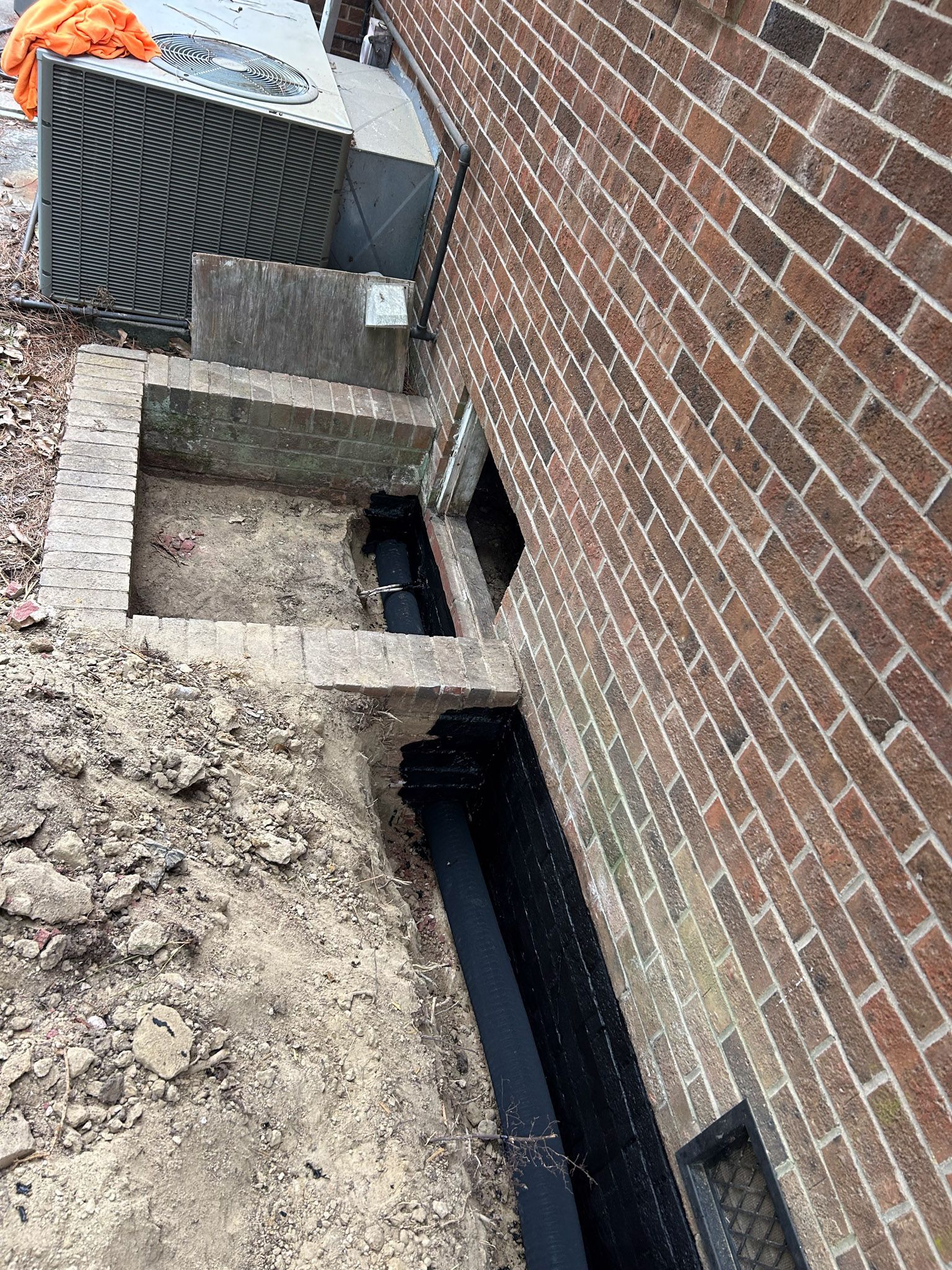Construction site: Brick building with excavated foundation, dark lining, and outdoor steps.