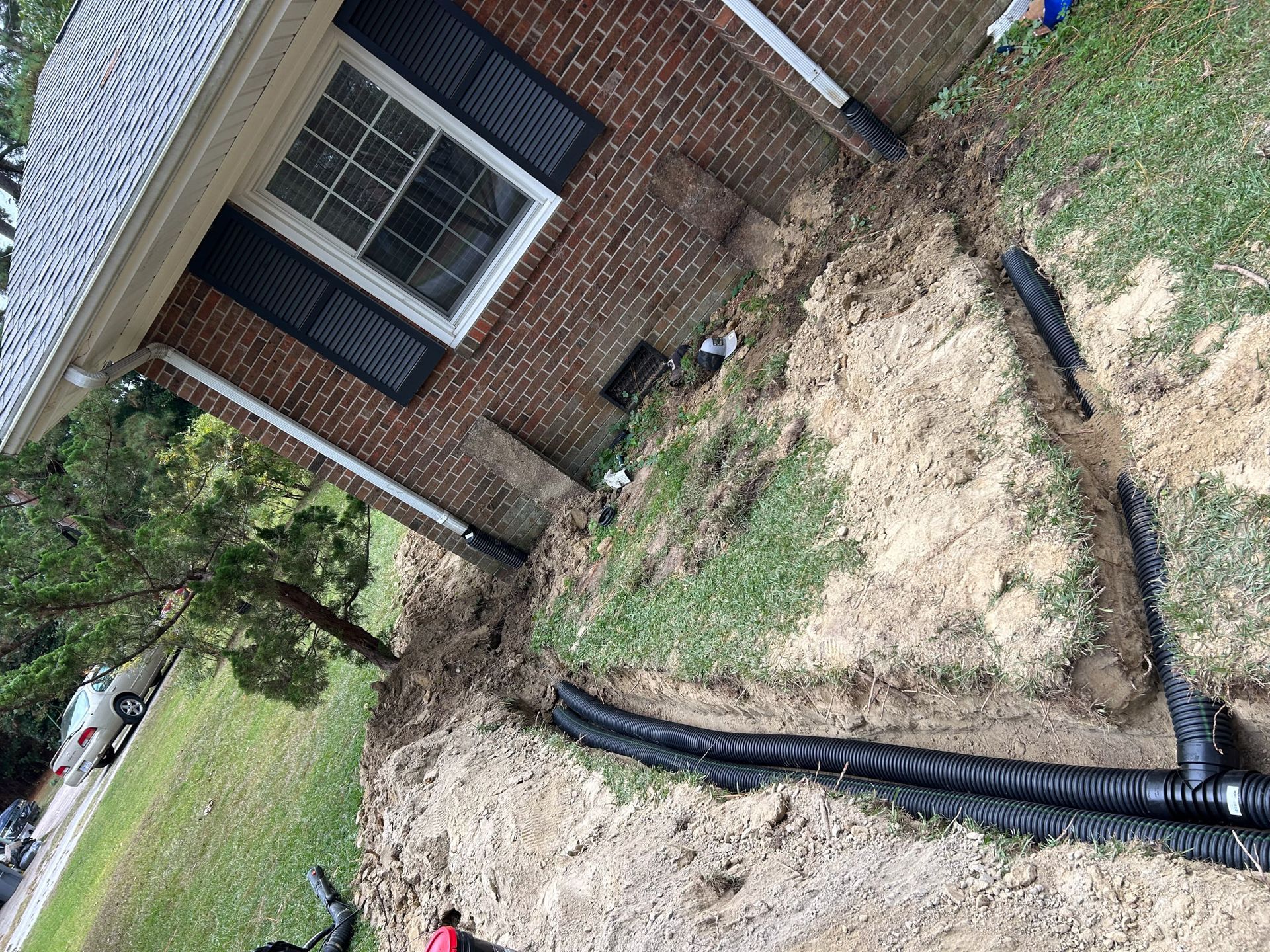 A house with a trench dug around it, filled with black drainage pipes.