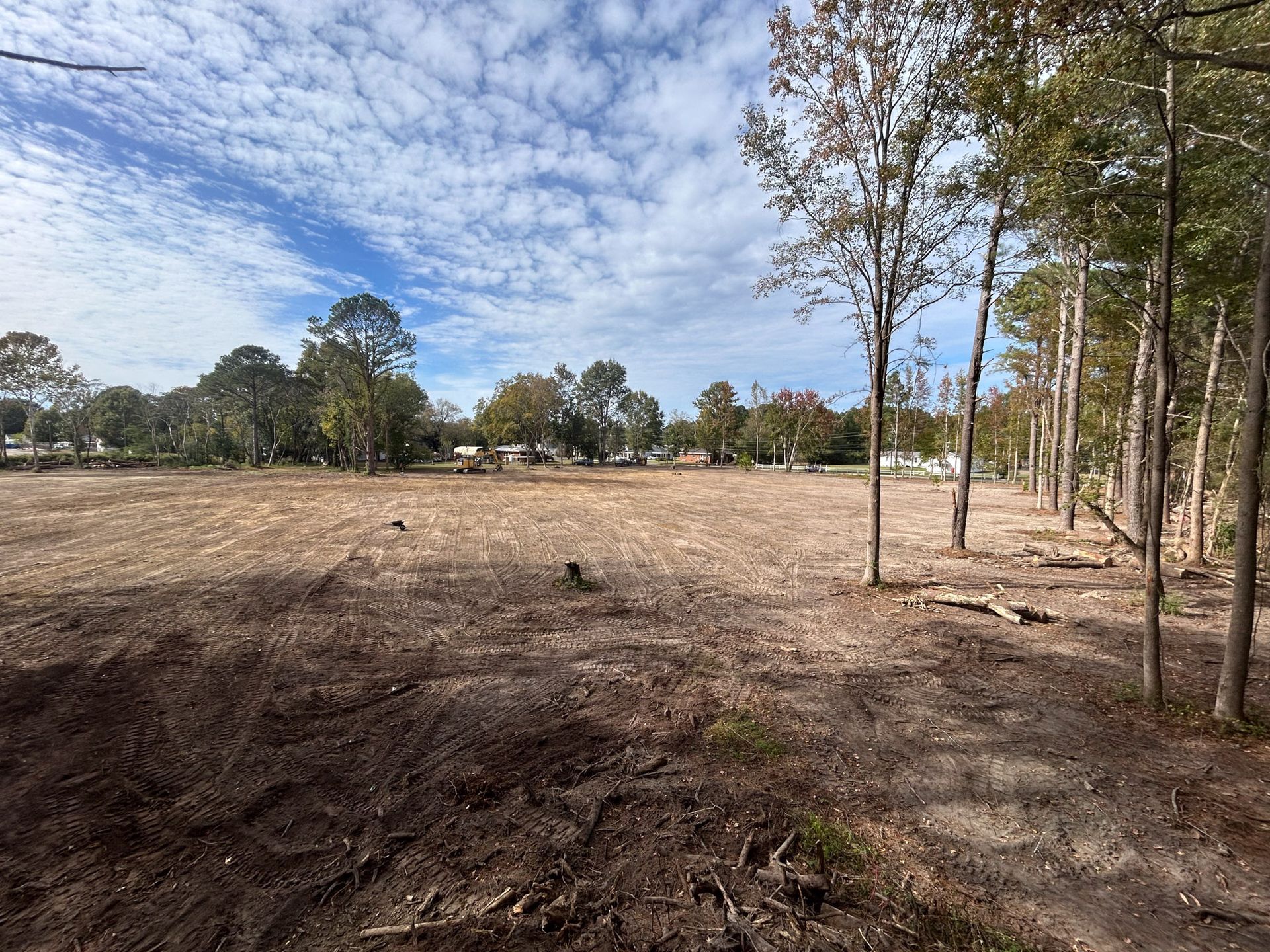A large, cleared field with scattered trees under a partly cloudy sky.