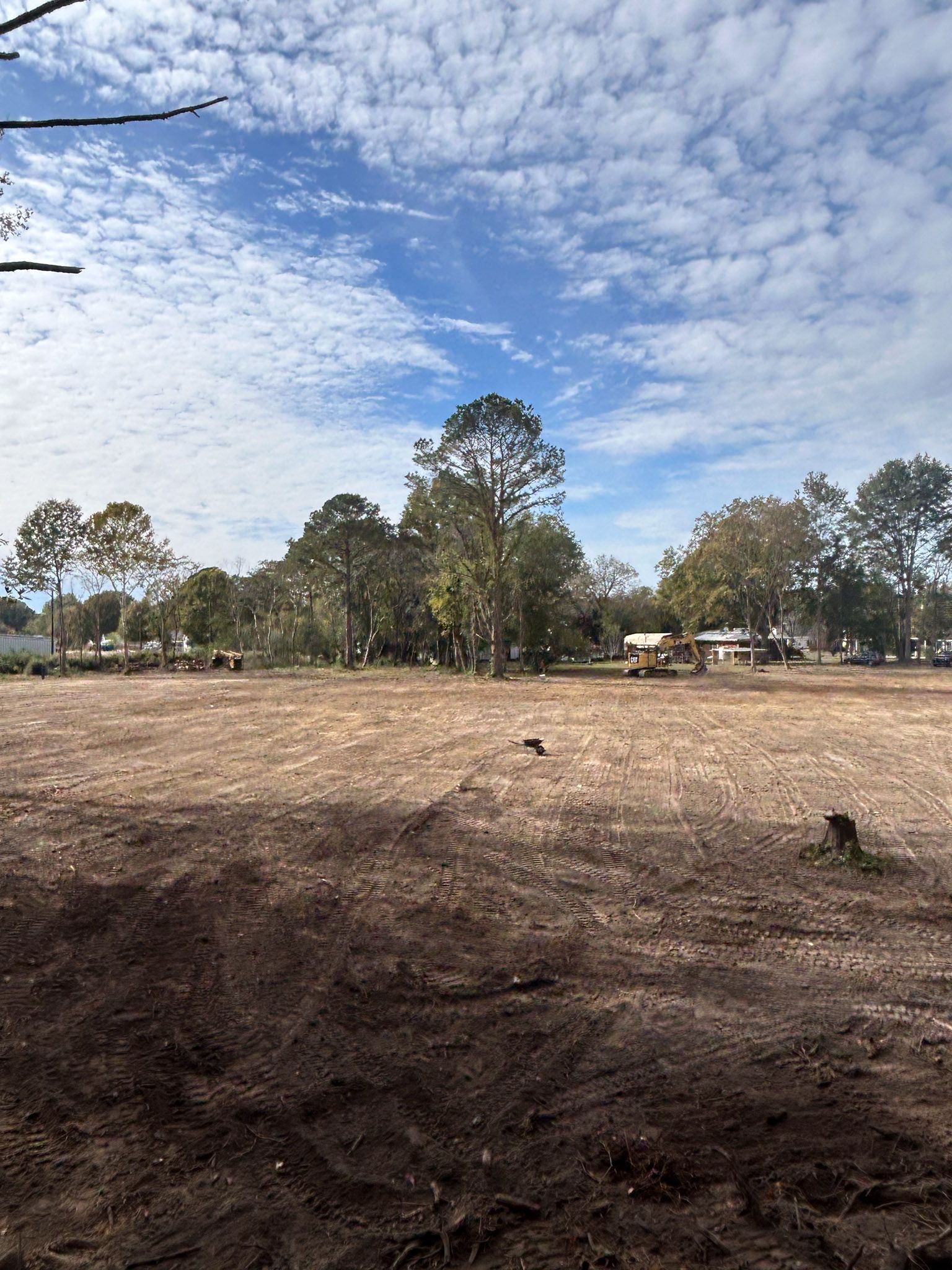 Cleared brown field with trees in the background under a partly cloudy sky.