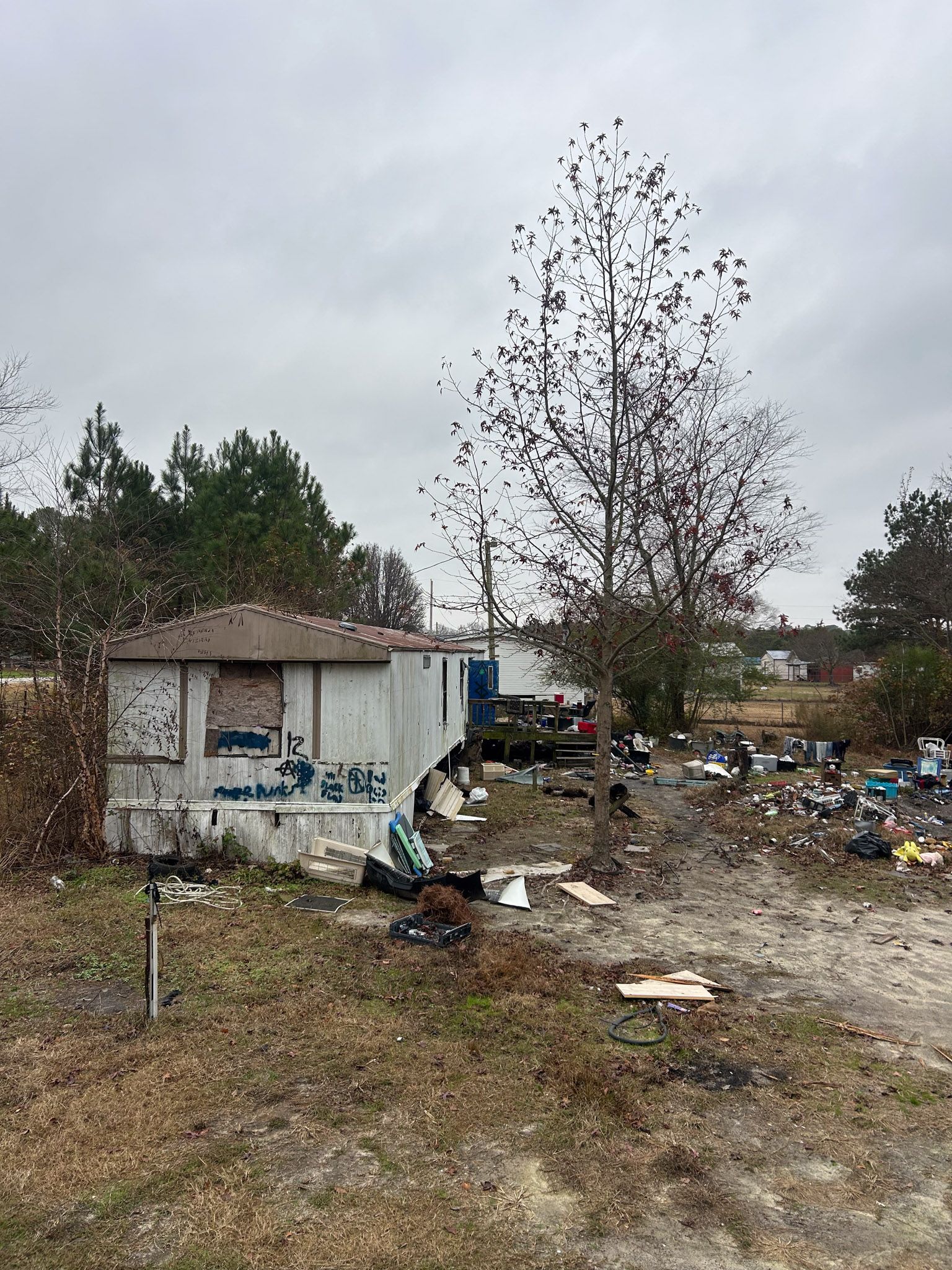 Dilapidated mobile home with surrounding debris and overcast sky.