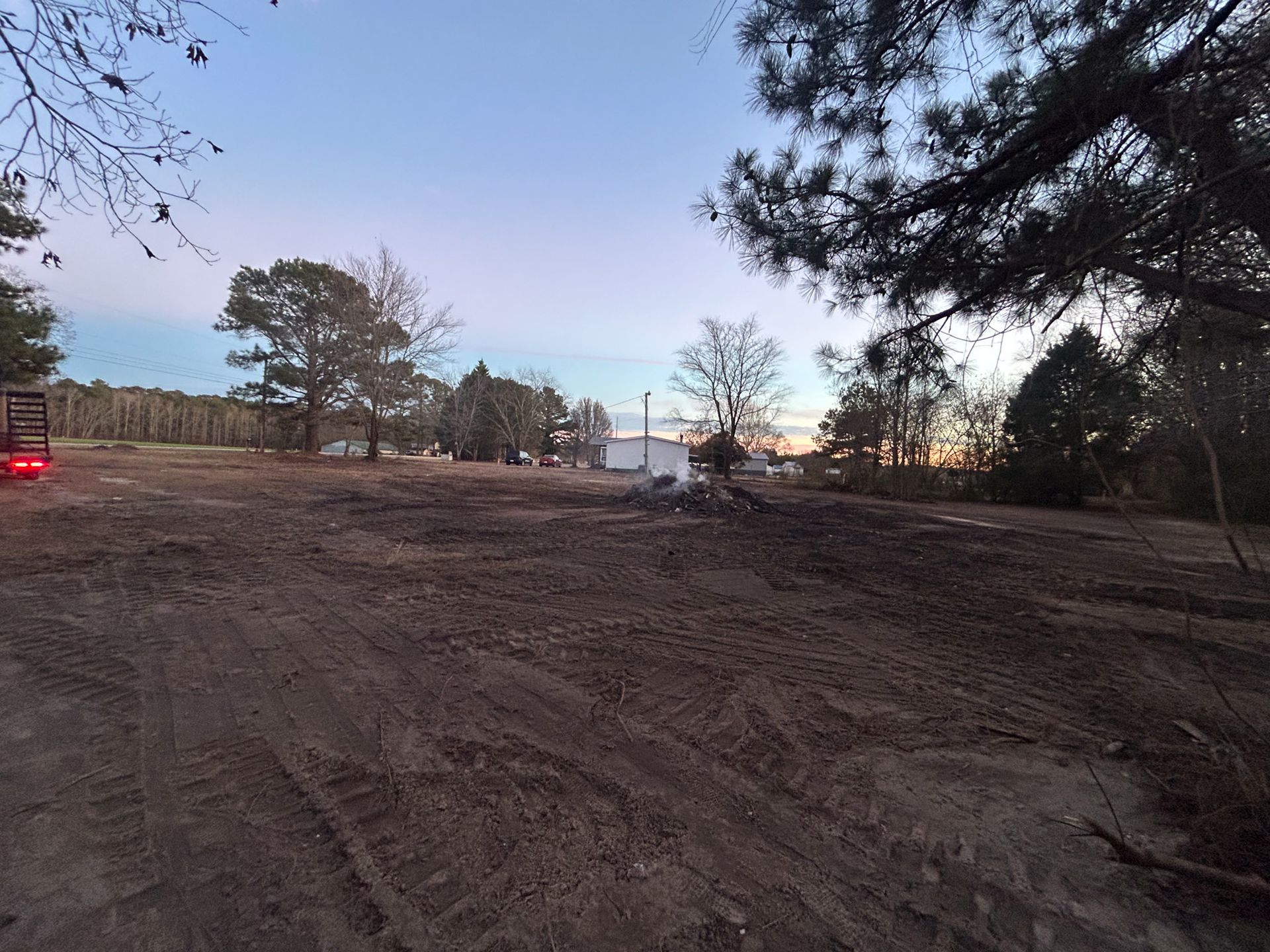 Clearing for construction: dirt field under a sunset sky with trees and a few buildings visible in the distance.