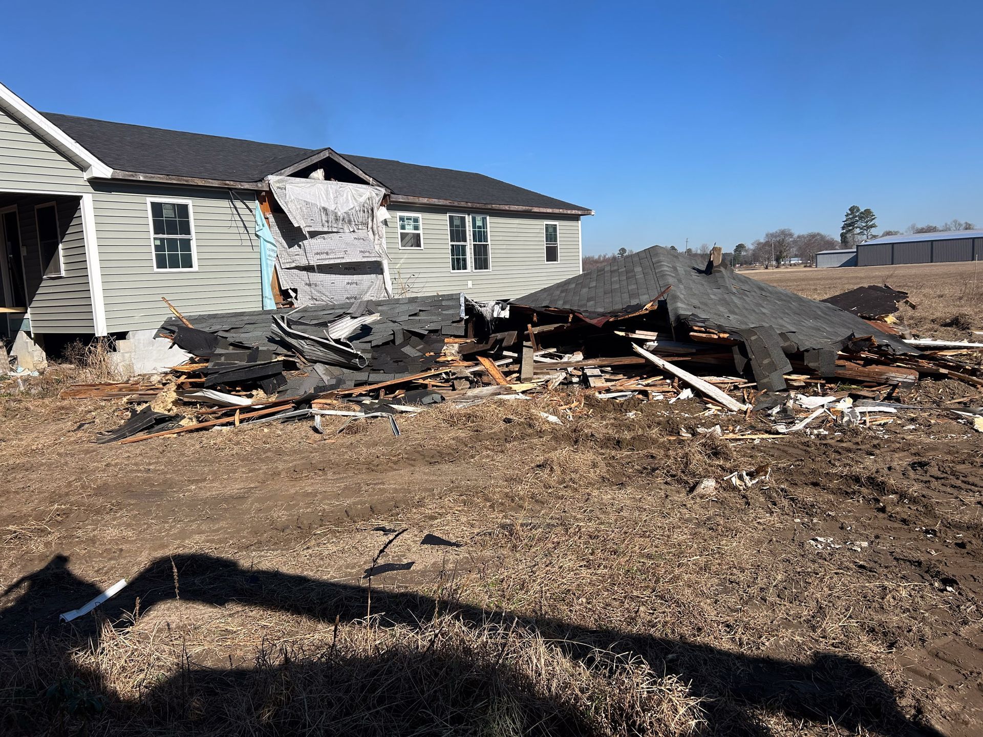 Partially collapsed house with debris on the ground; sunny, outdoor setting.