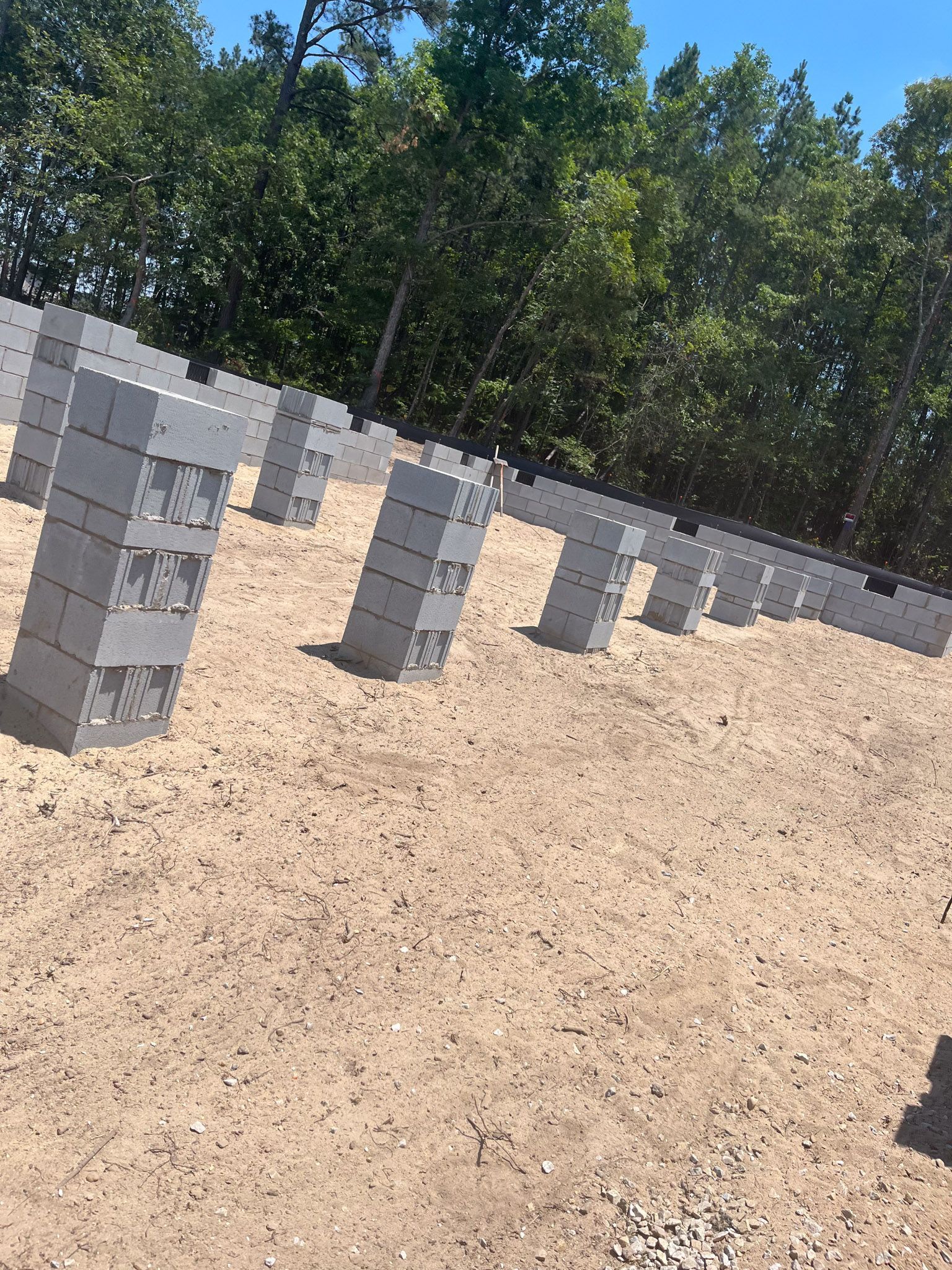 Rows of gray cinder block columns on a dirt foundation, trees in the background.