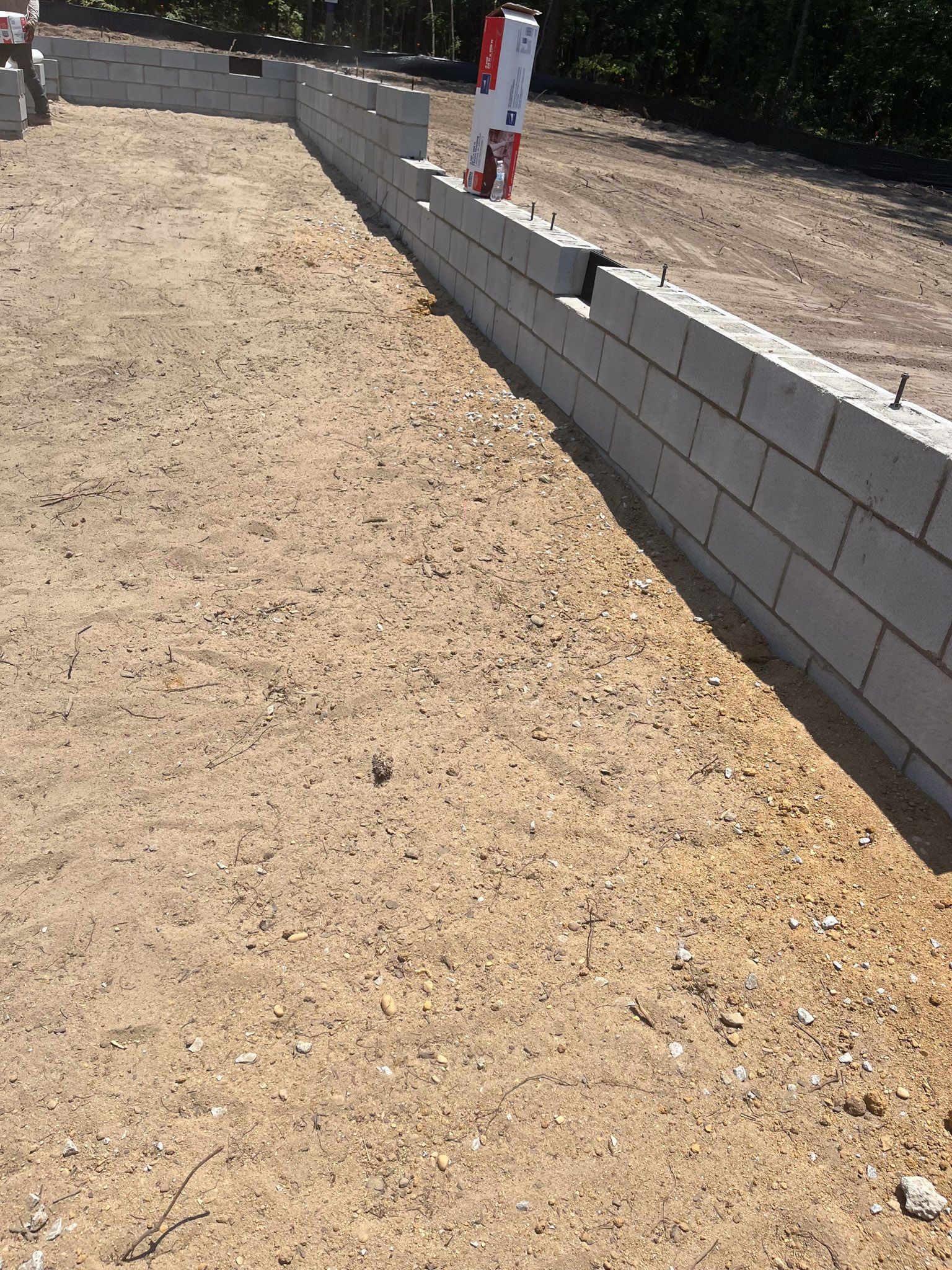 Concrete block foundation construction on a dirt lot. Red and white level tool present.