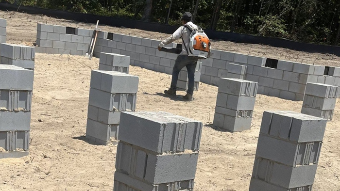 Person using a backpack leaf blower on a construction site with stacked cinder blocks.