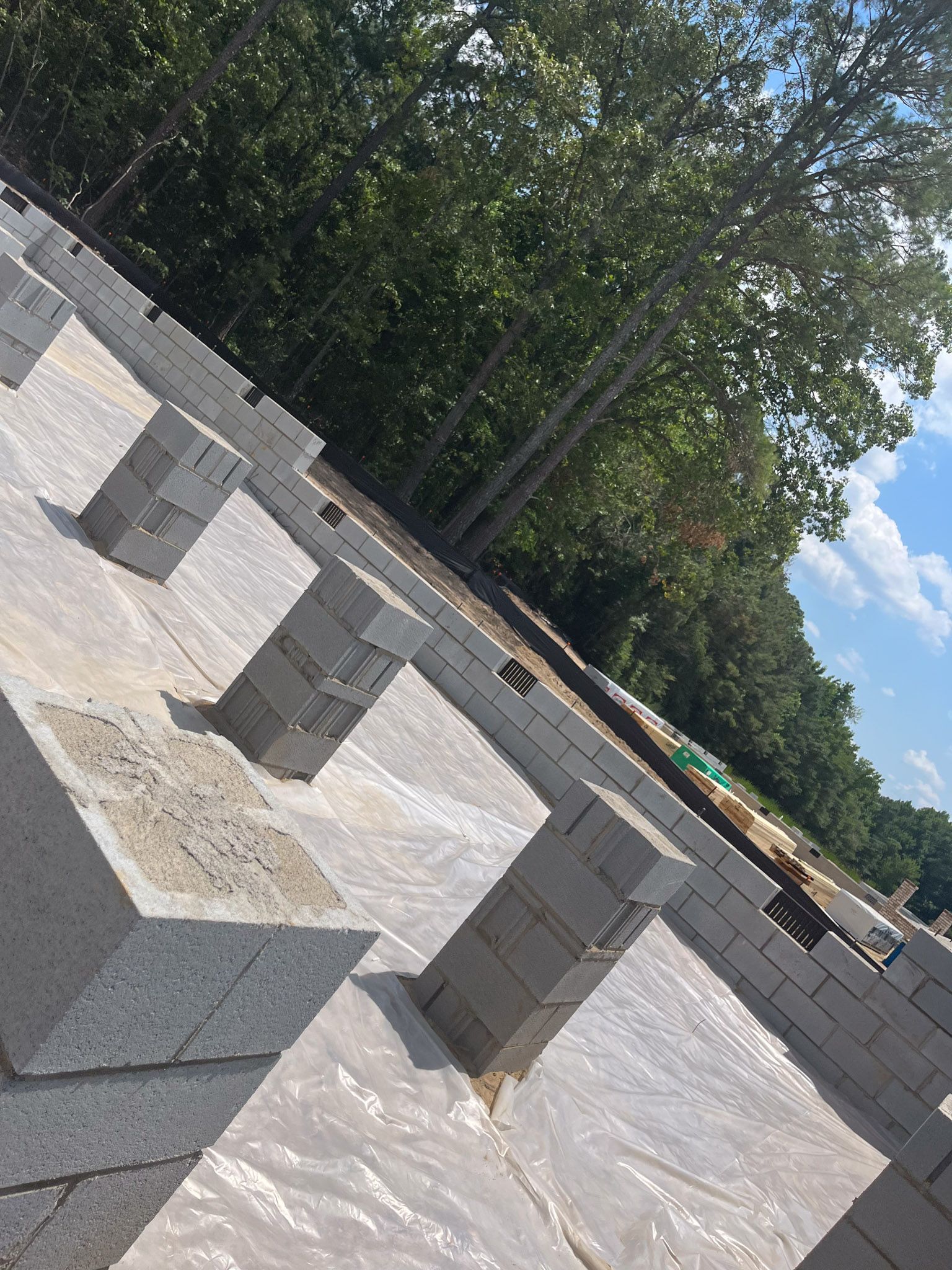 Concrete blocks forming foundation on a construction site, with plastic sheeting and trees in background.