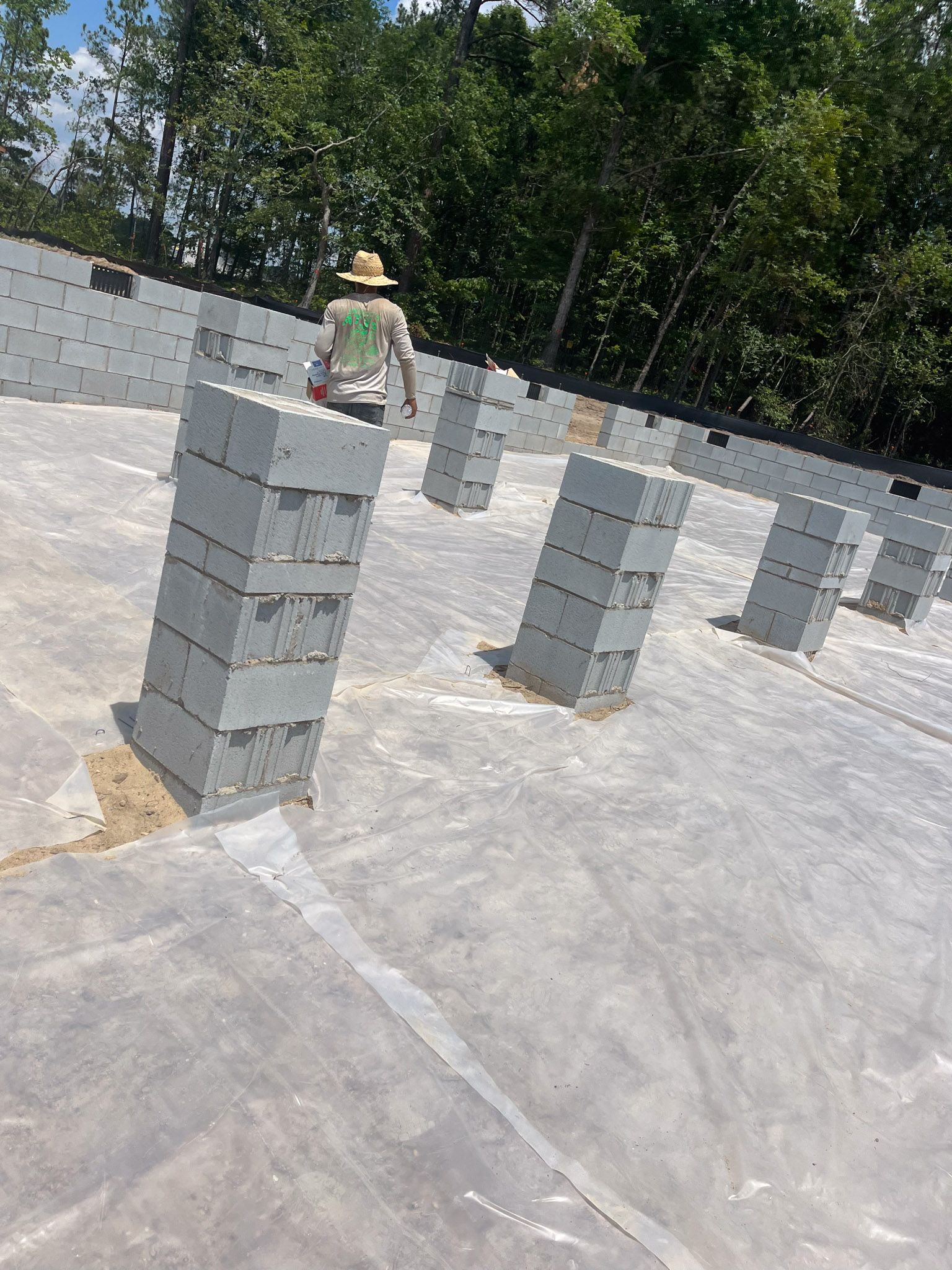 Construction worker on a rooftop with stacked gray cinder blocks. Trees in the background.