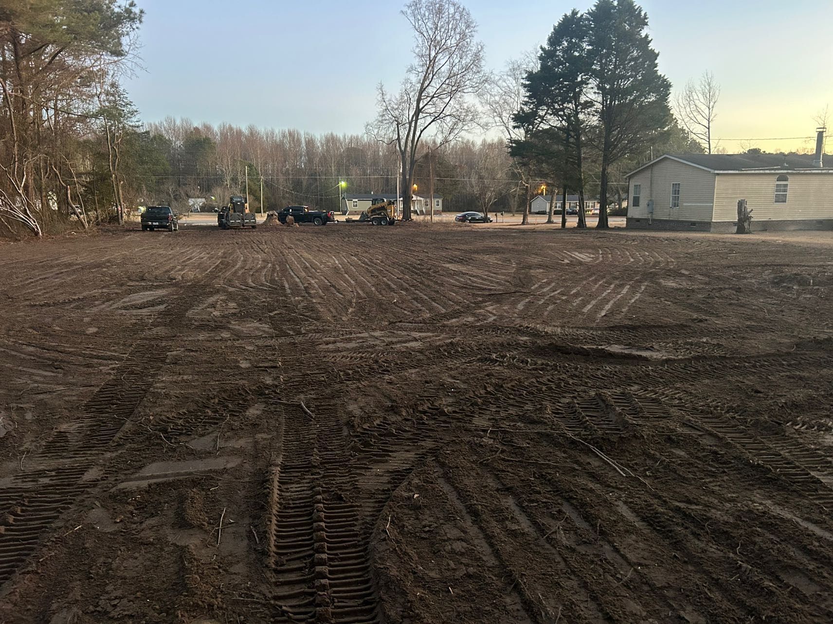 Muddy, cleared field with tractor tracks, trees in background, small building on right.