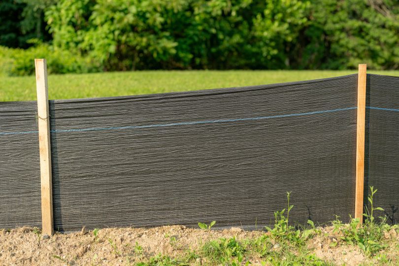 Black silt fence between two wooden posts, protecting a grassy area.