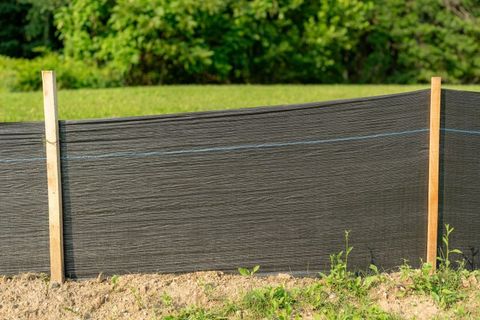 Black silt fence between two wooden posts, protecting a grassy area.