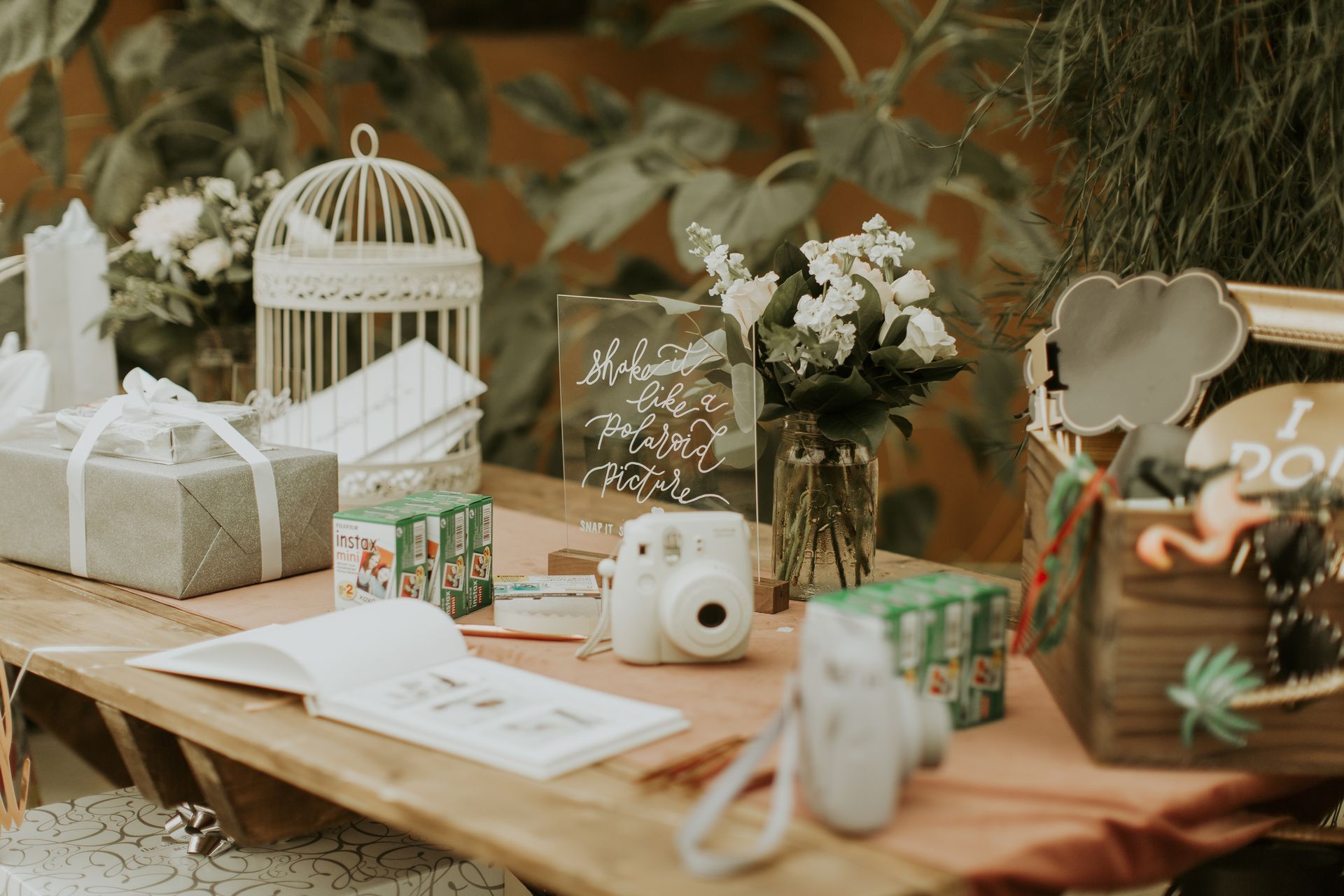 A wooden table topped with a book, a camera, a bird cage , and flowers.