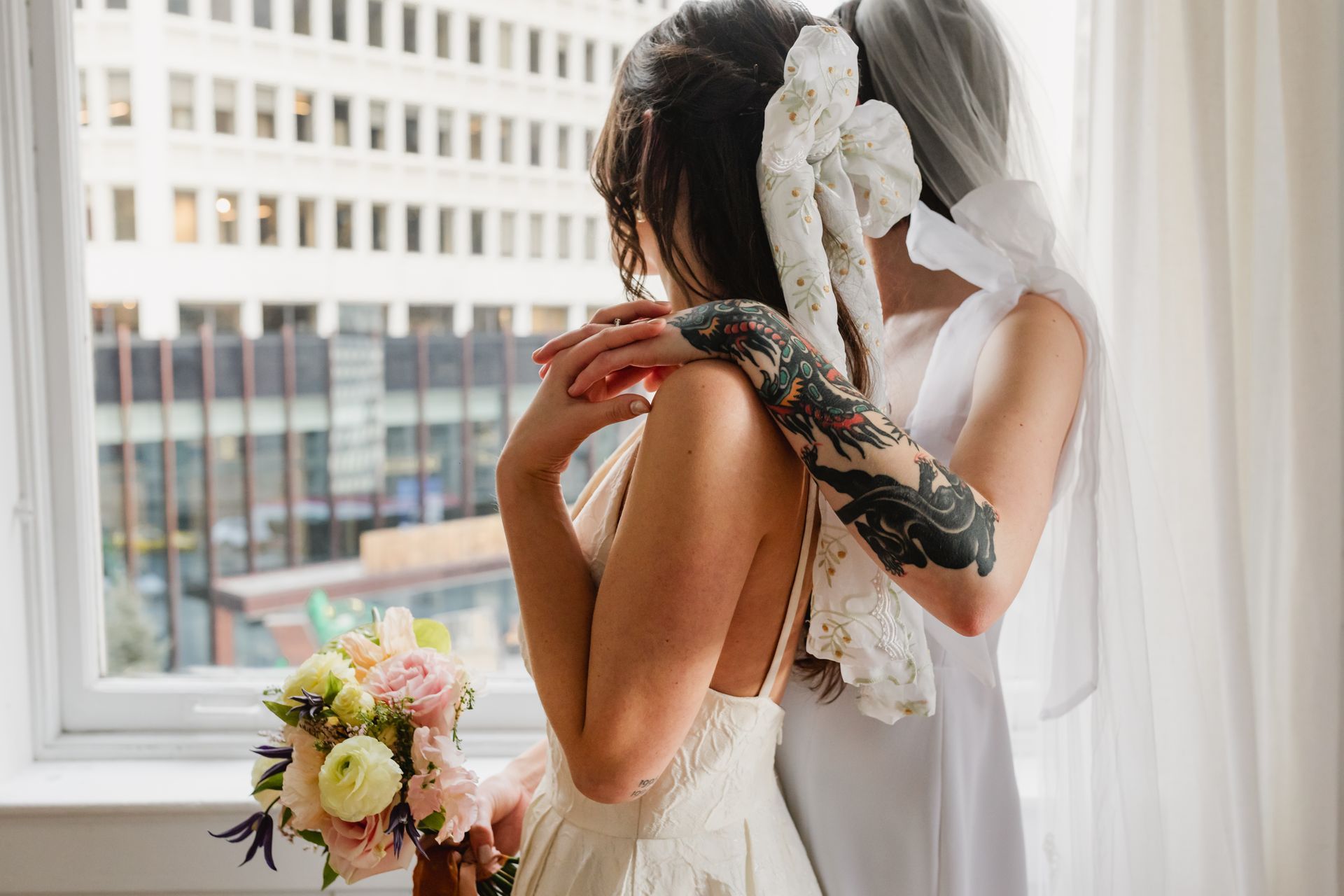 two brides looking out of the window, one has a bow in their hair and the other has bows on their dress