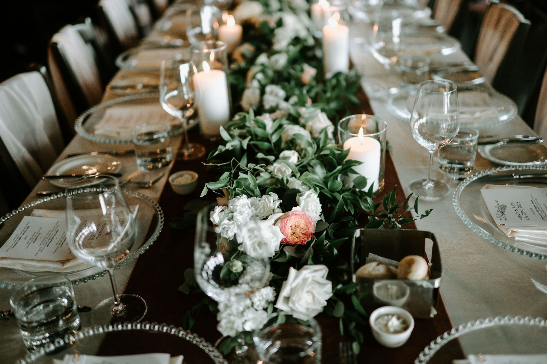 table dressed with glass chargers and flower running down the centre of the table, blush velvet table runner