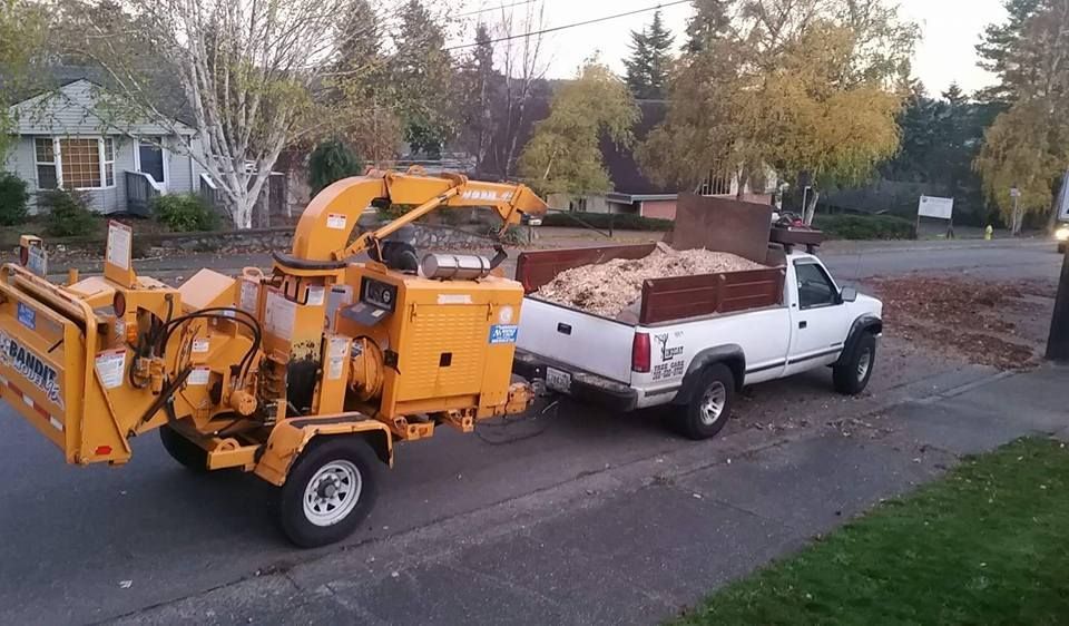 A white truck with a wood chipper attached to it.