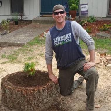A man is kneeling next to a tree stump with a plant in it.