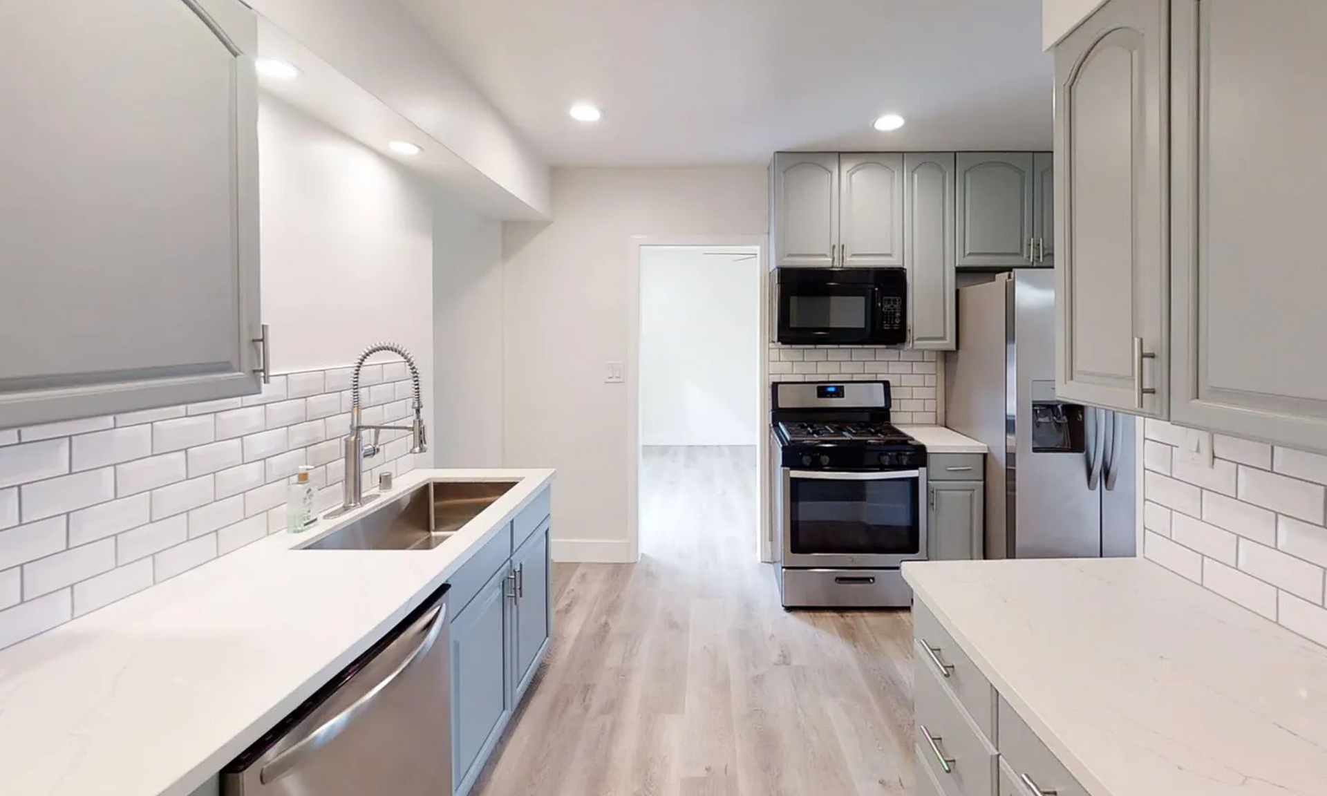 Gray and white kitchen with stainless steel appliances and light wood flooring.