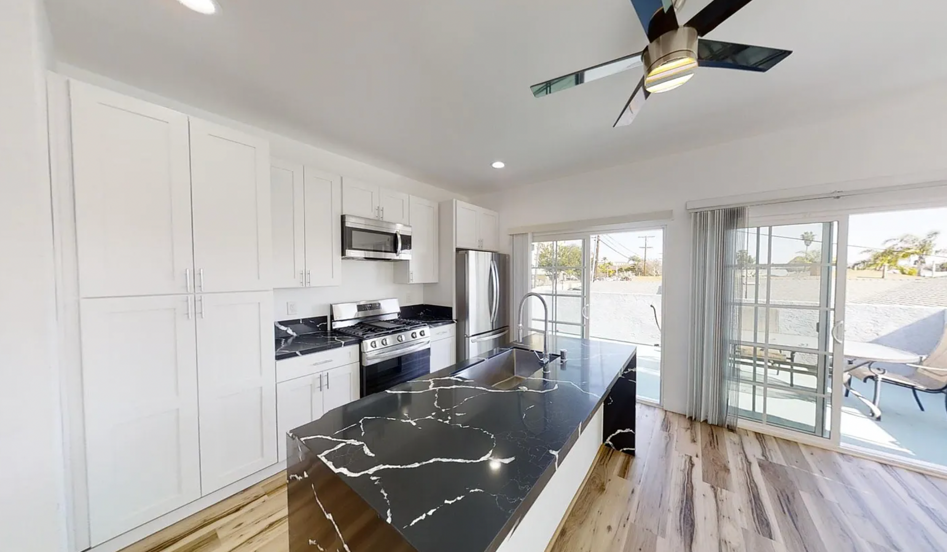 Bright kitchen with white cabinets, black countertop island, stainless steel appliances, and sliding glass doors to a patio.