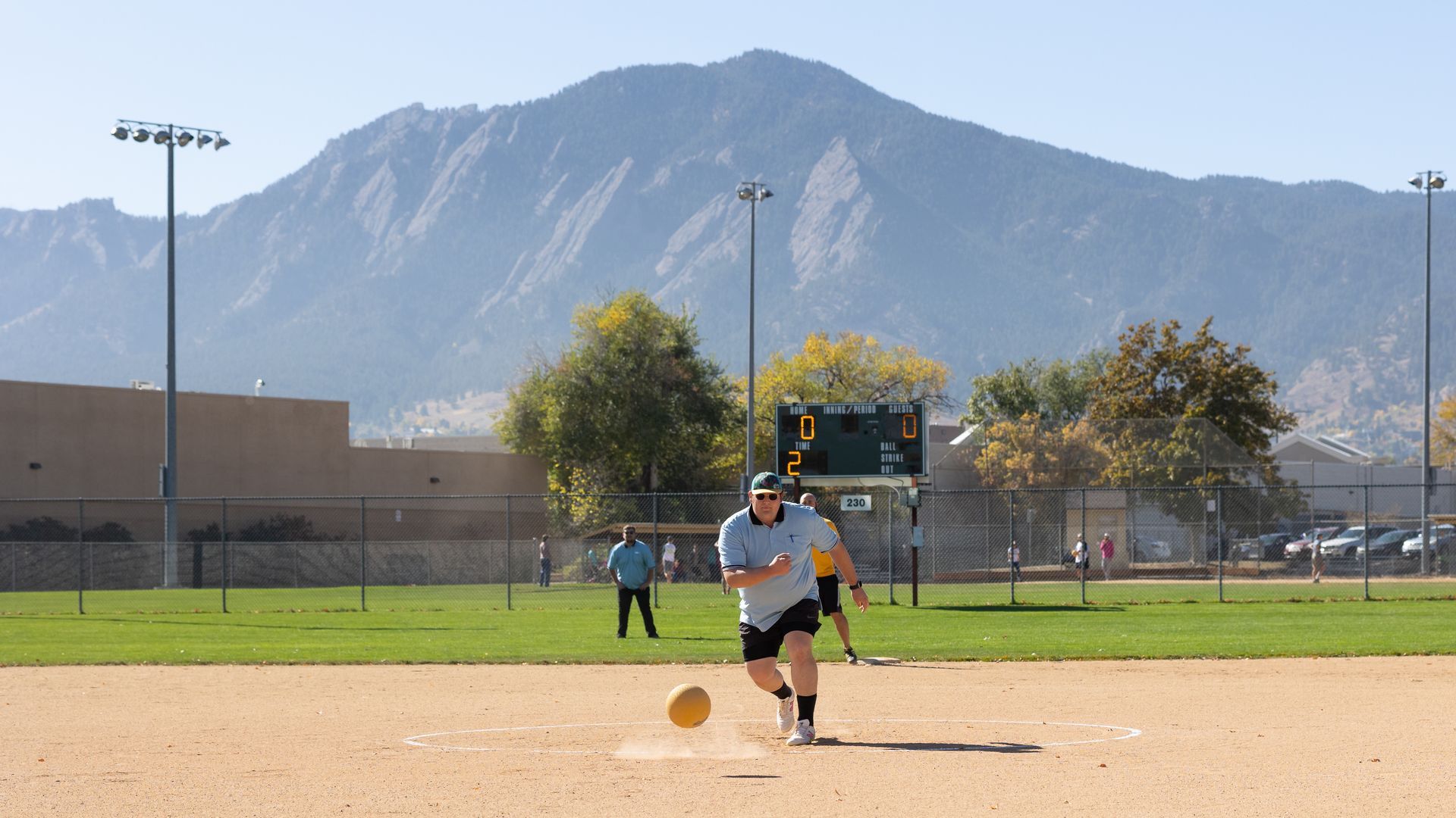 Person kicking a ball on a baseball field, mountain in background.